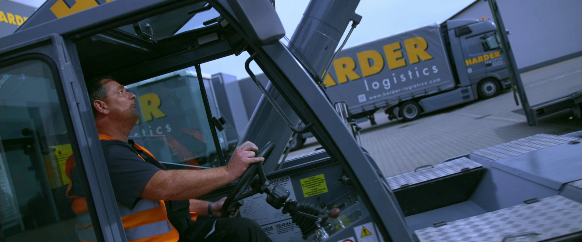 Imagefilm der Filmproduktion Panda Pictures aus München und Ulm für HARDER. Ein Darsteller sitzt in der Fahrerkabine eines Gabelstaplers, ein Harder-Lkw fährt im Hintergrund. Nahaufnahme der Tätigkeit.