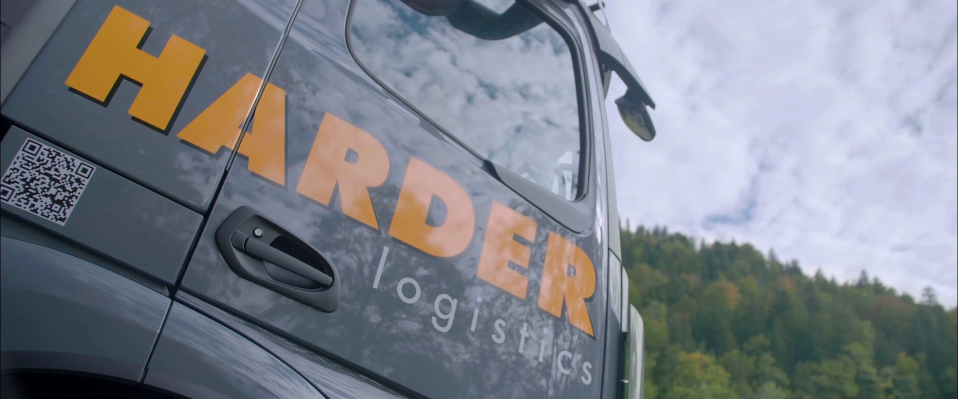 Imagefilm der Filmproduktion Panda Pictures aus München und Ulm für HARDER. Seitenansicht eines Harder-Lkws mit Logo und QR-Code vor Berglandschaft. Die Szene ist ideal für eine Imagefilm-Produktion.