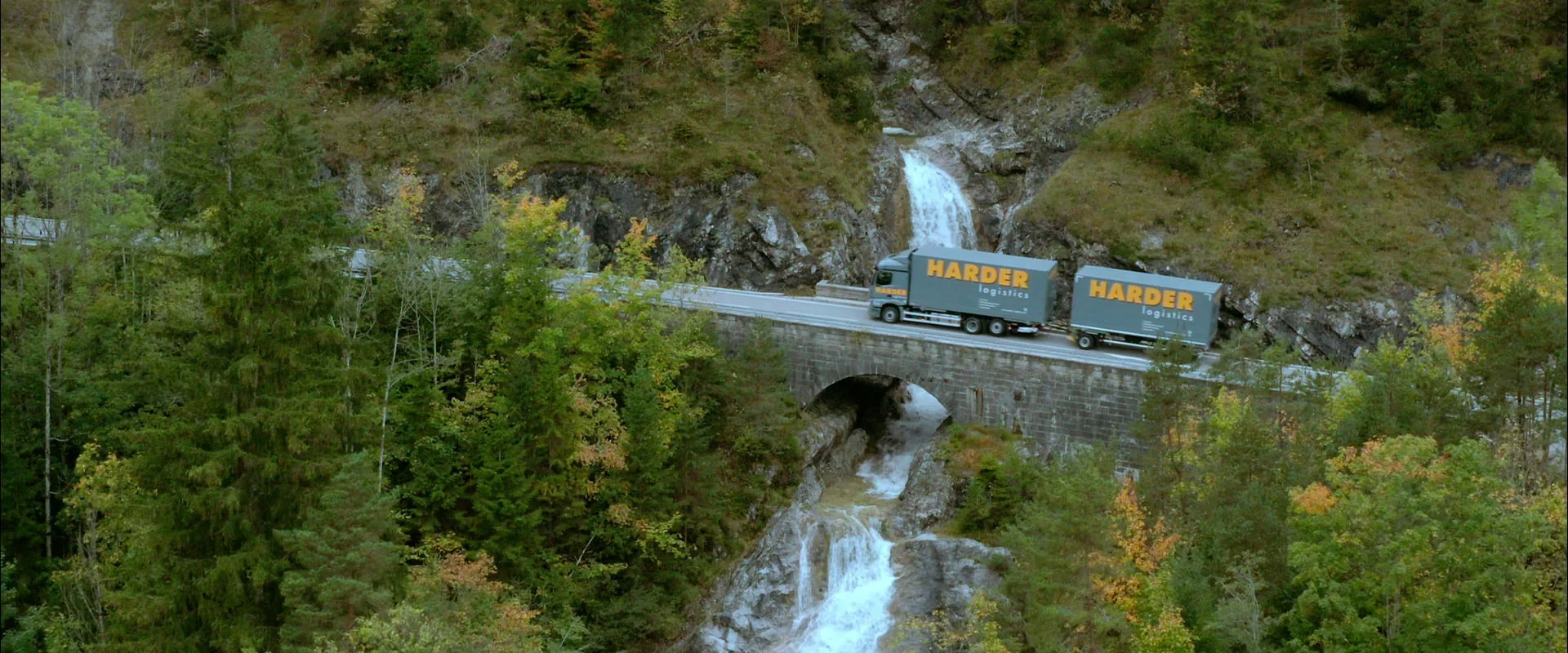 Imagefilm der Filmproduktion Panda Pictures aus München und Ulm für HARDER. Ein Harder-Lkw fährt über eine Brücke mit Wasserfällen im Herbstwald. Eine malerische Landschaftsaufnahme für den Film.