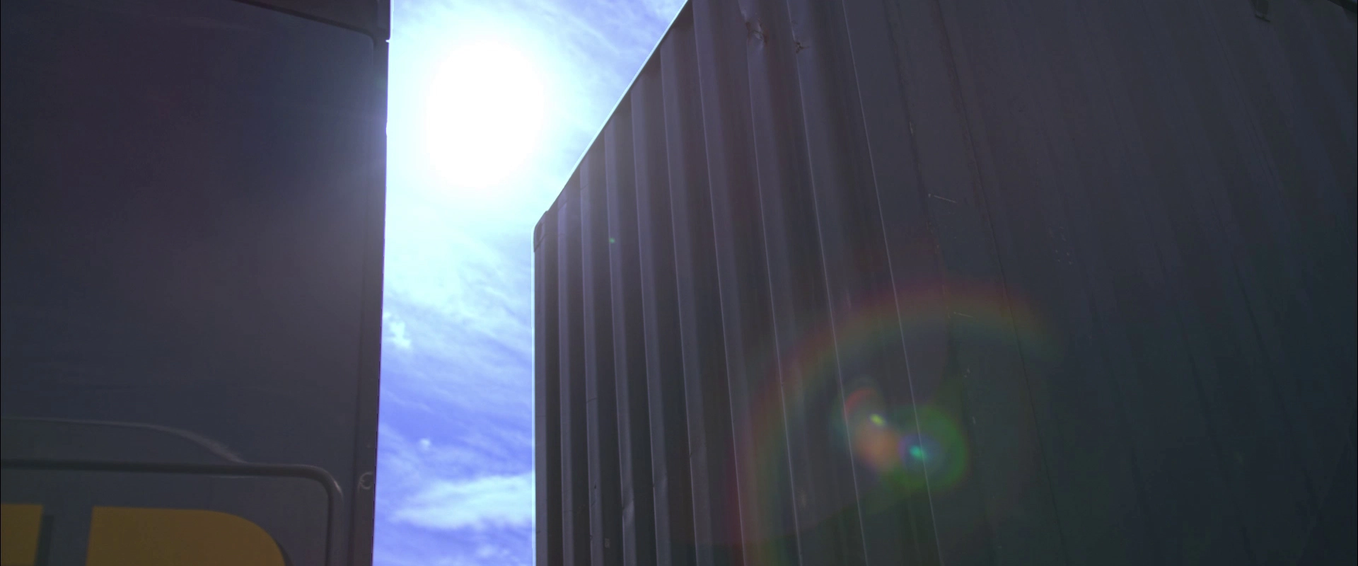 Imagefilm der Filmproduktion Panda Pictures aus München und Ulm für HARDER. Die Sonne scheint hell zwischen zwei Containern hindurch, mit deutlichem Lens Flare. Ein kunstvoller Effekt der Postproduktion.