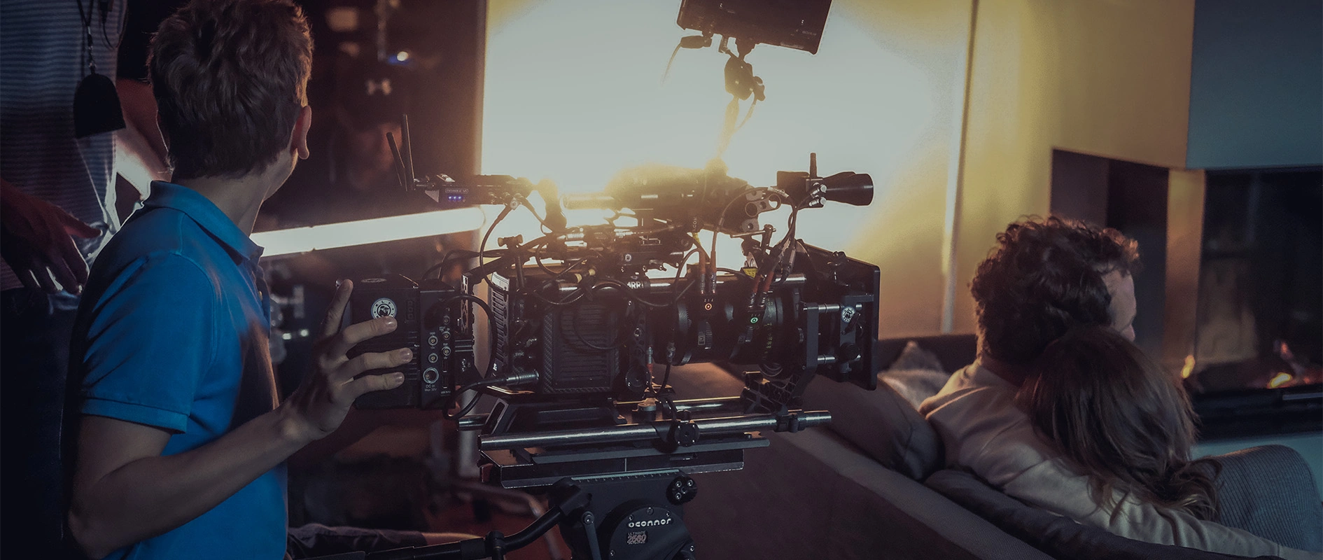 Imagefilm der Filmproduktion Panda Pictures aus München und Ulm für Scheuermann & Heilig. Ein Drehteam arbeitet an einer Szene in einem Wohnzimmer, wobei ein Techniker die Beleuchtungseinstellungen an der professionellen Kamera anpasst.