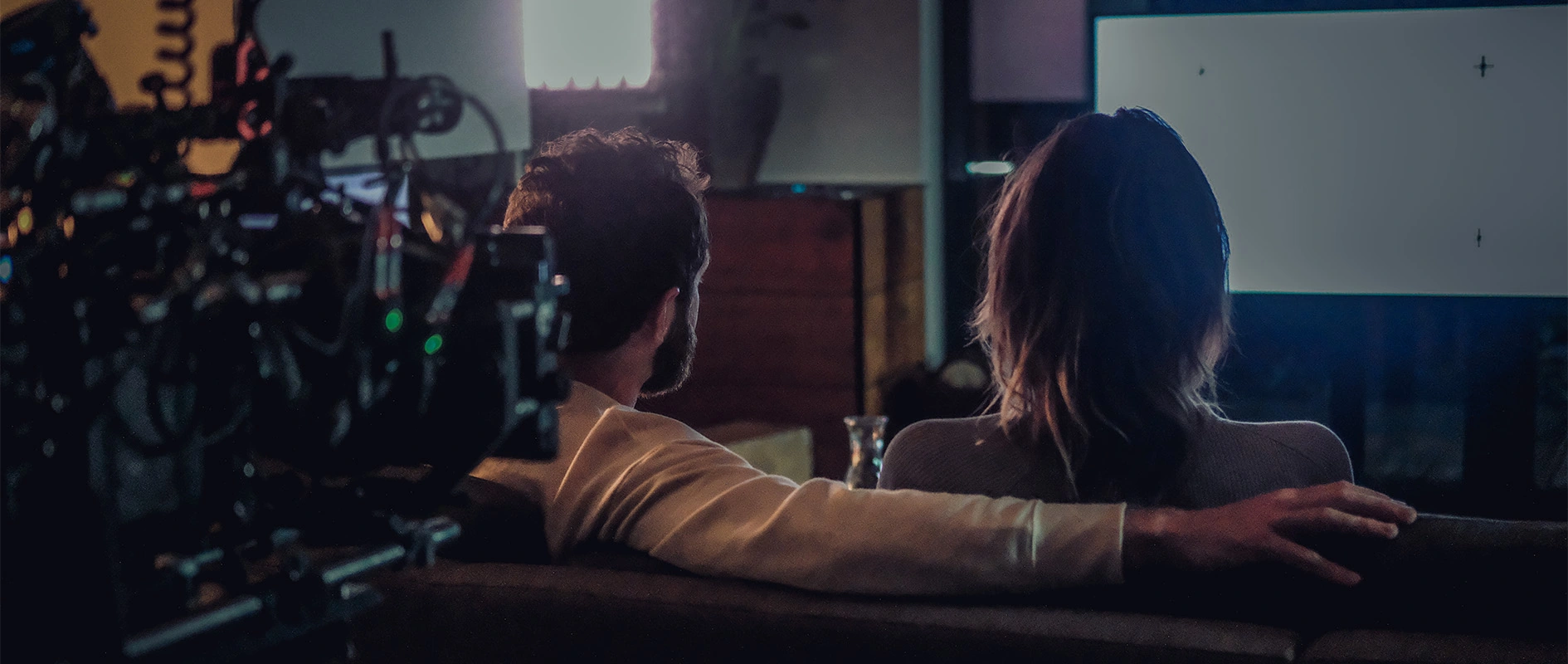 Imagefilm der Filmproduktion Panda Pictures aus München und Ulm für Scheuermann & Heilig. Eine Szene wird gedreht, in der zwei Darsteller auf einem Sofa sitzen und auf einen unsichtbaren Bildschirm blicken, während die Kamera im Vordergrund steht.