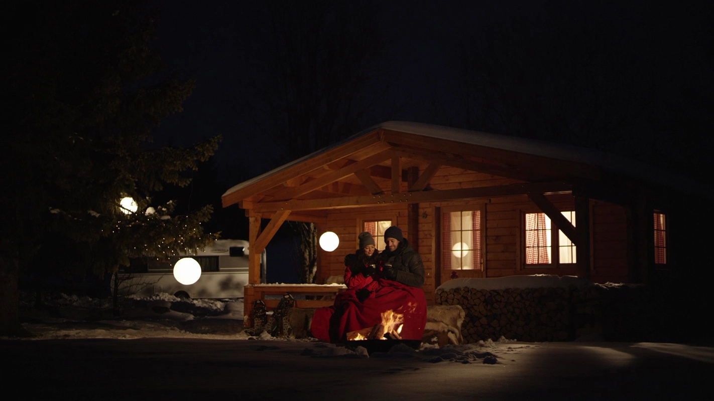 Filmproduktion Panda Pictures aus München und Ulm zum Thema Filmproduktion in München. Ein Paar sitzt am Lagerfeuer vor einer Hütte im Schnee. Die richtige Lichtsetzung ist bei Dreharbeiten in der Nacht entscheidend für eine romantische Atmosphäre.