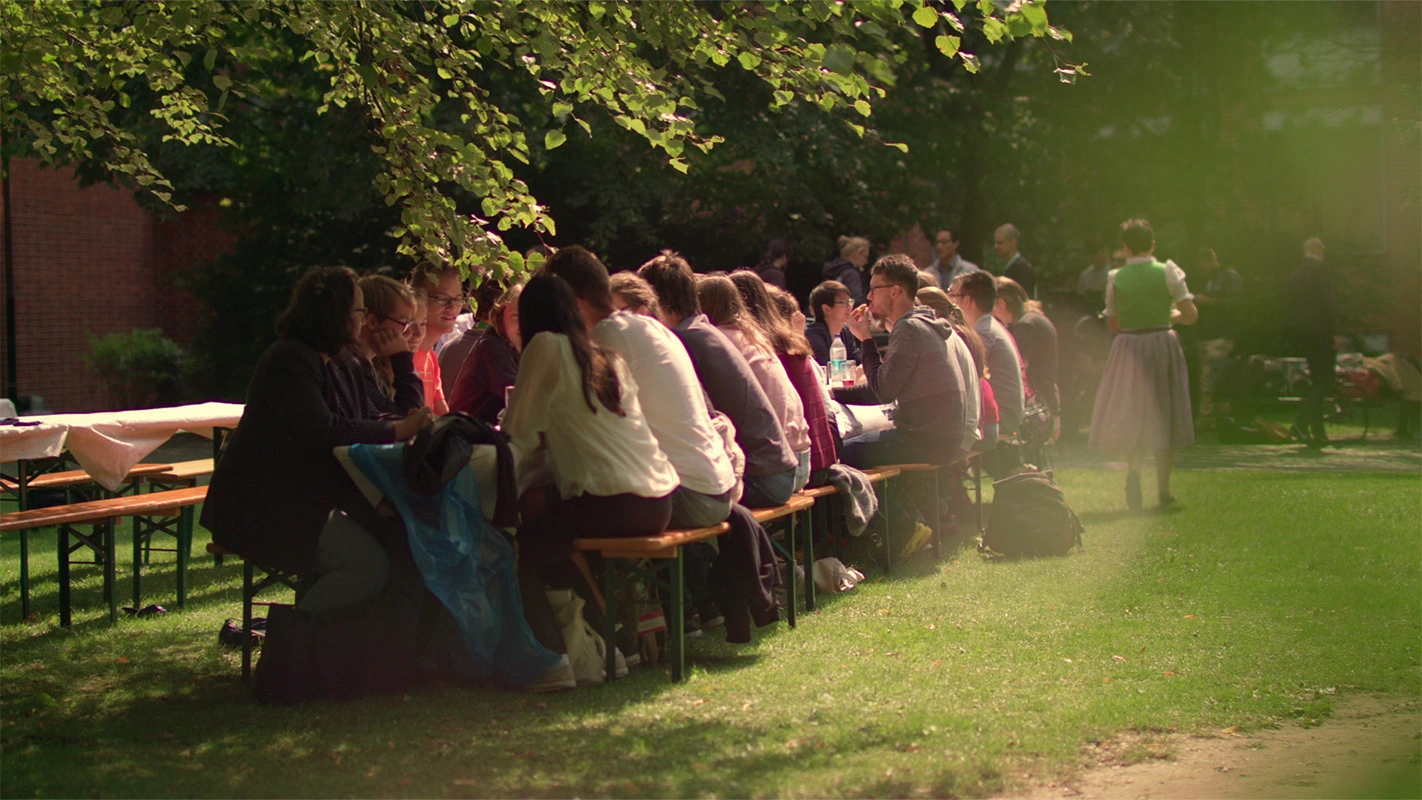 Filmproduktion Panda Pictures aus München und Ulm zum Thema Filmproduktion in München. Menschen sitzen an Biertischen in einem sonnigen Park. Die Dreharbeiten fangen das authentische Lebensgefühl der Stadt München und seiner Gärten ein.