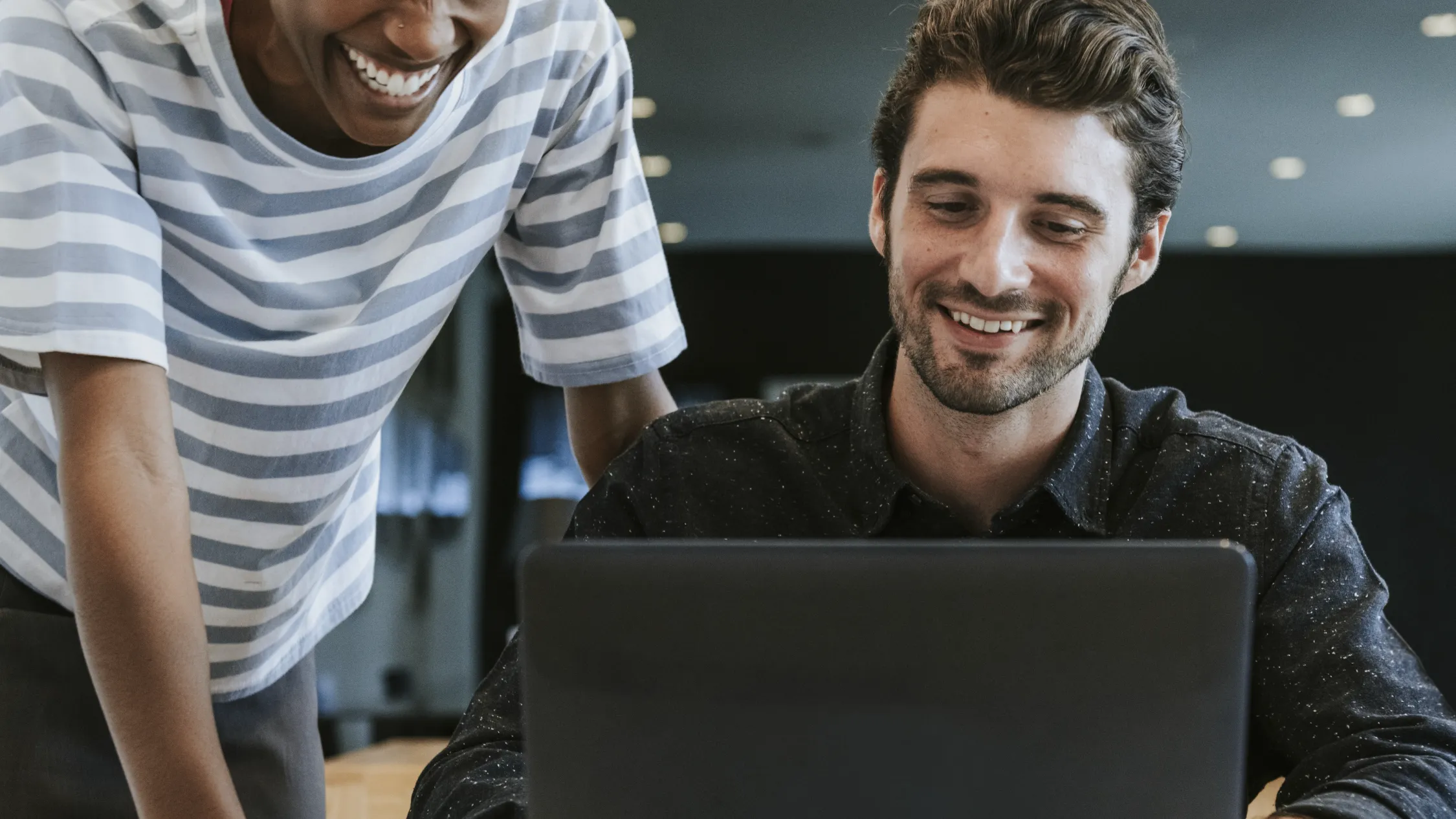 Onboarding mit der Filmproduktion Panda Pictures aus München und Ulm.  Ein Mitarbeiter arbeitet den anderen ein. Beide lachen.