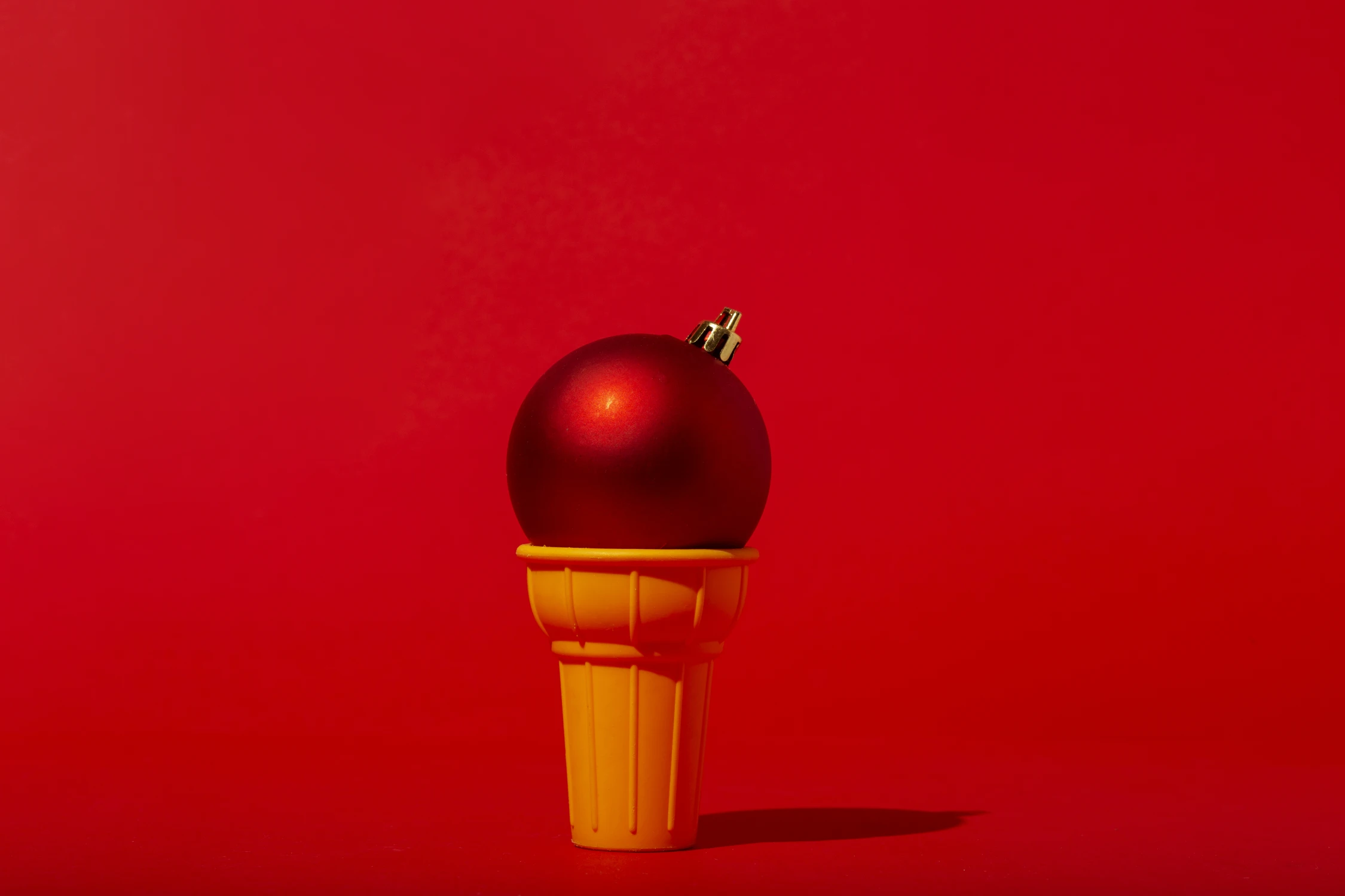 Rote Weihnachtskugel auf einem gelben Waffelkegel vor einem lebhaften roten Hintergrund, die kreative Weihnachtswerbung-Ideen von Panda Pictures in Filmproduktion und Videoproduktion in München und Ulm zeigt.