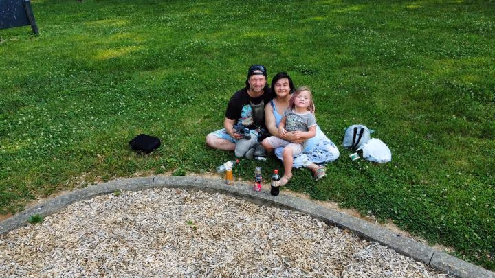 A man, woman and child sit on a grassy field.