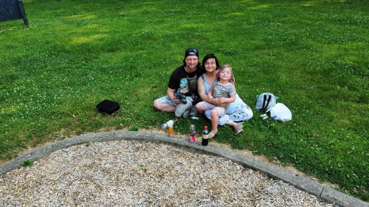 A man, woman and child sit on a grassy field.
