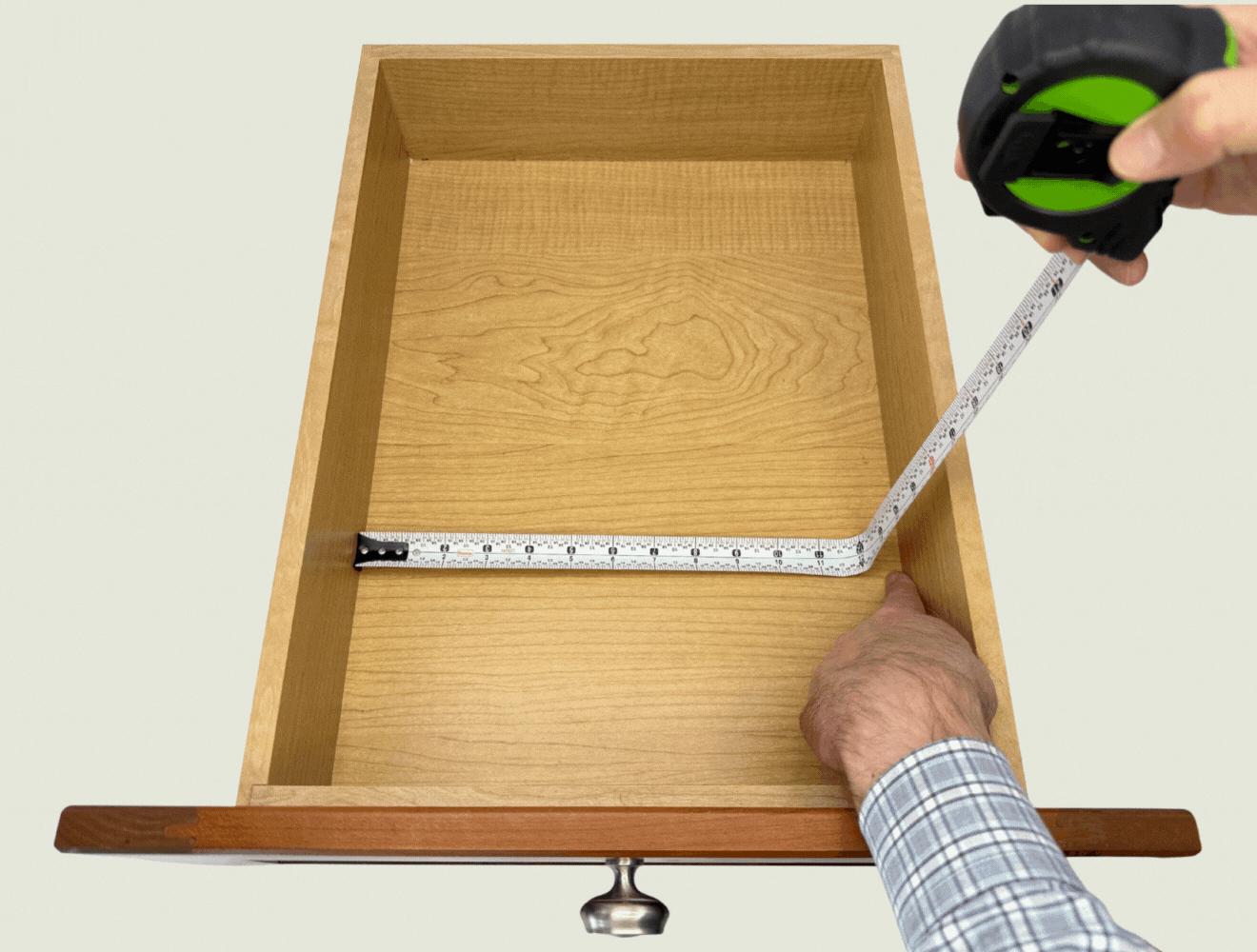 Animated image showing a person using a tape measure to record the interior dimensions of an empty wooden drawer, capturing both width and depth.