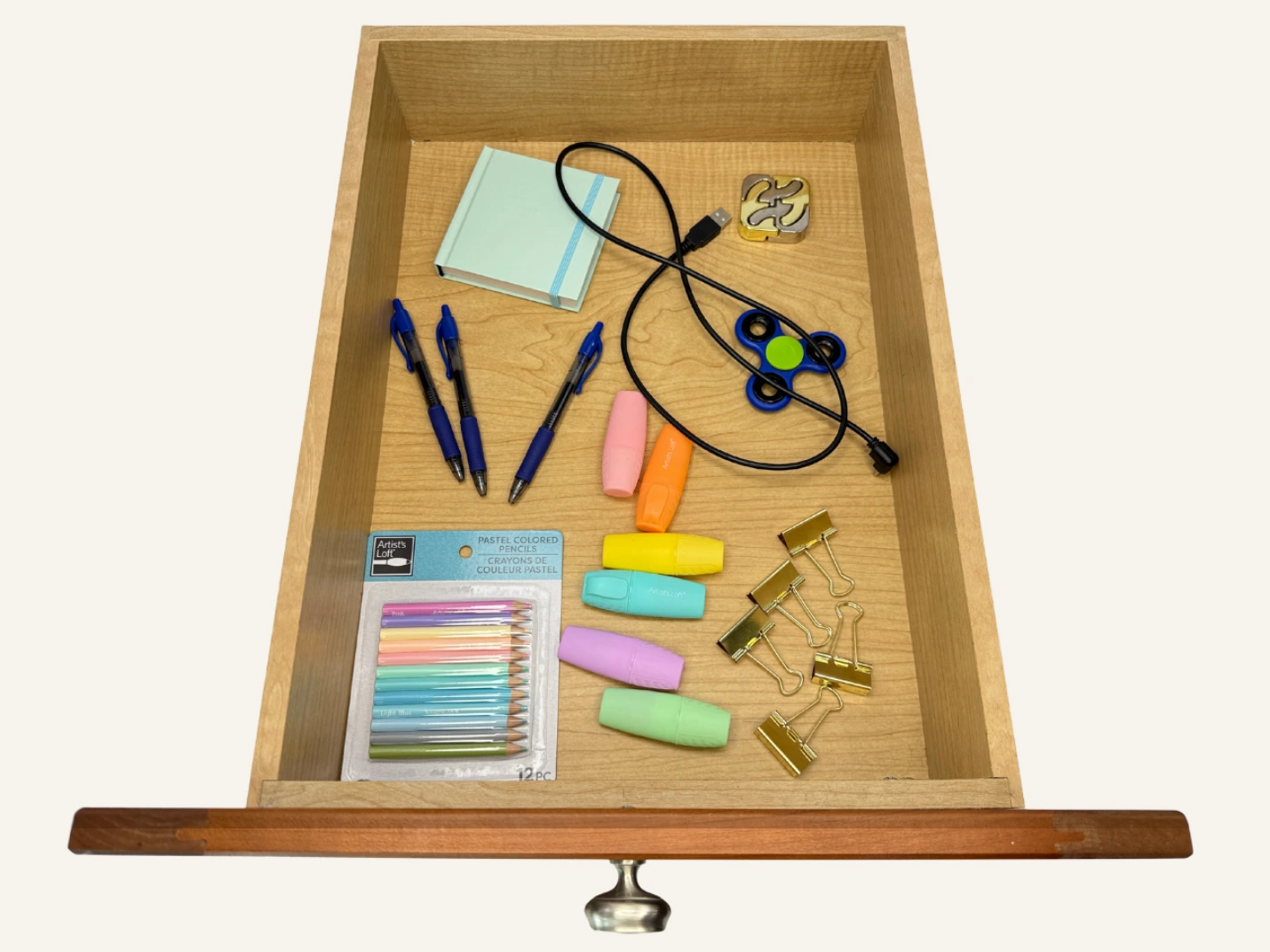 Open drawer with white custom compartments containing orange scissors, two green-handled screwdrivers, four blue pens, and a closed light blue notebook.