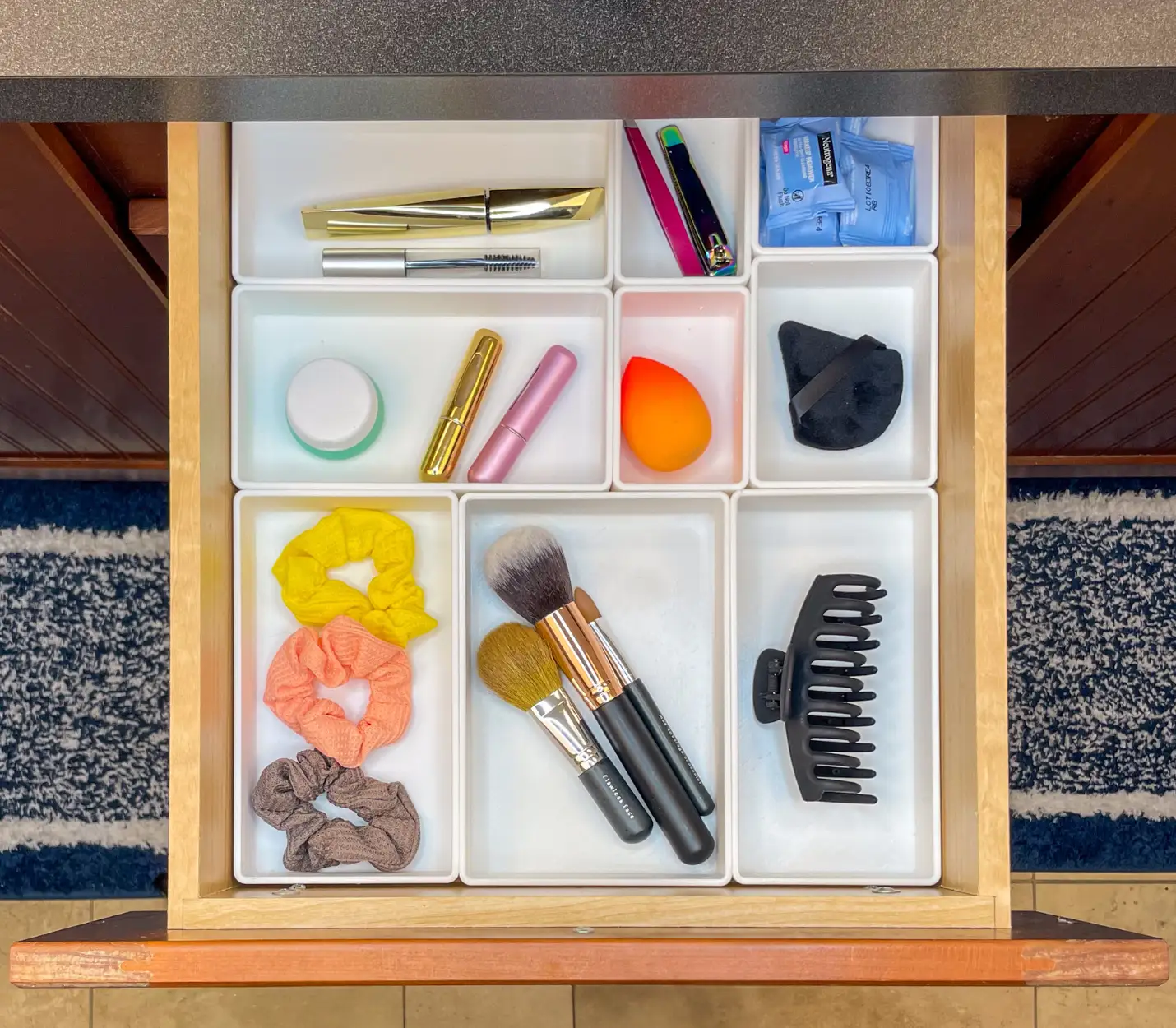 Top-down view of a bathroom drawer with white custom trays neatly organizing makeup, hair ties, brushes, a hair clip, and grooming items.