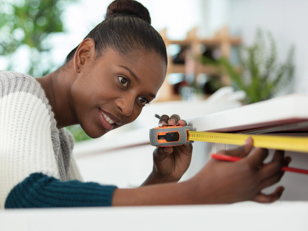 Woman measuring the interior of a drawer with a tape measure and pencil, preparing for drawer organization or customization.