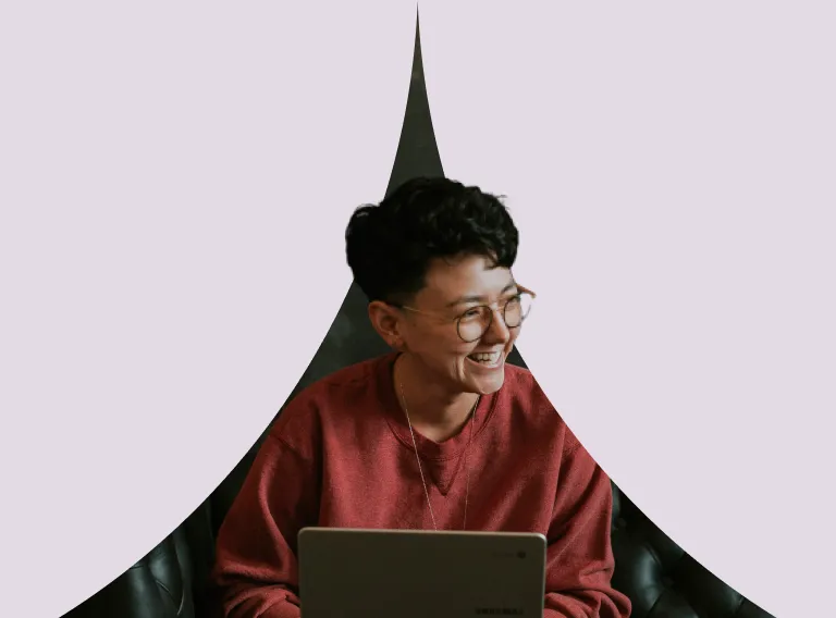 A man with glasses is smiling while using a laptop.