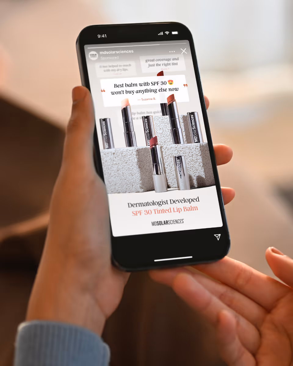 A hand holding an iPhone displaying an Instagram ad of a skincare brand.