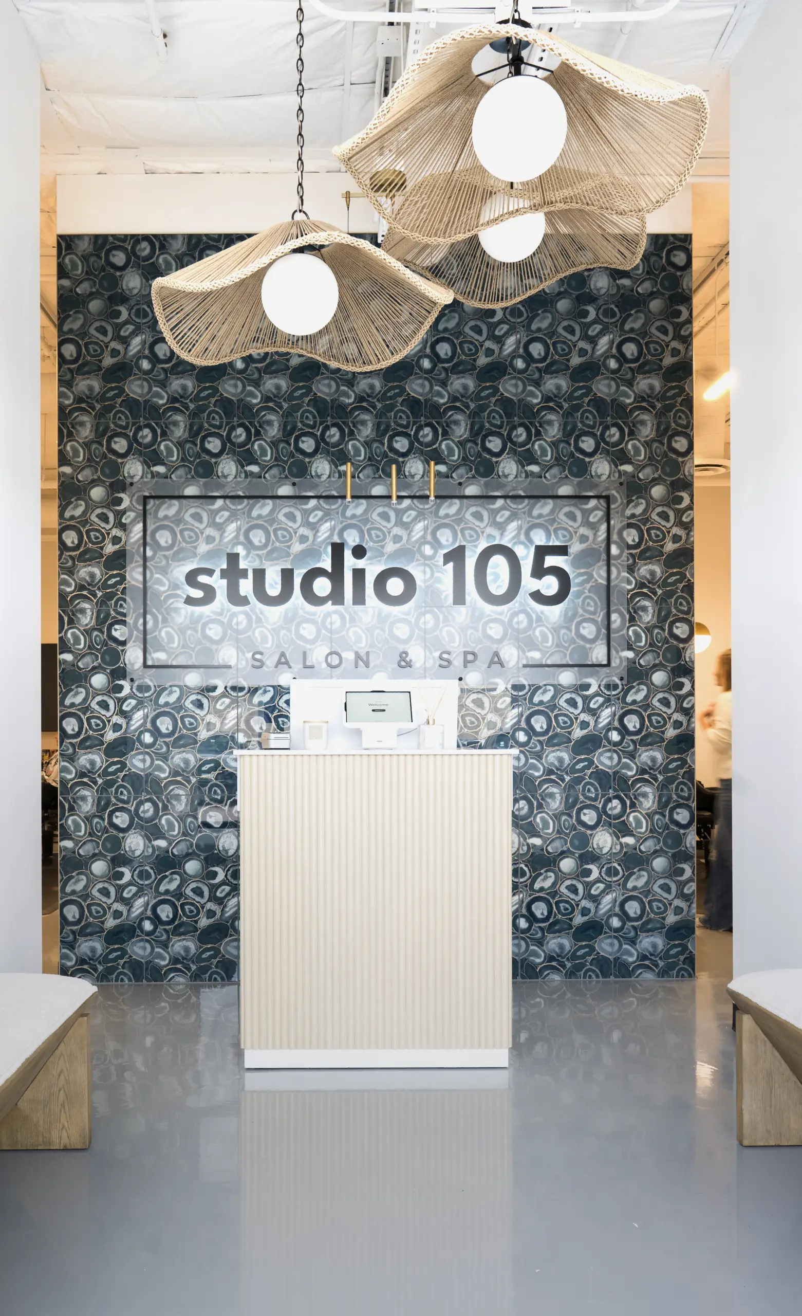 Reception area of Studio 105 Salon & Spa with a modern white front desk, blue patterned wall, and large wicker pendant lights.