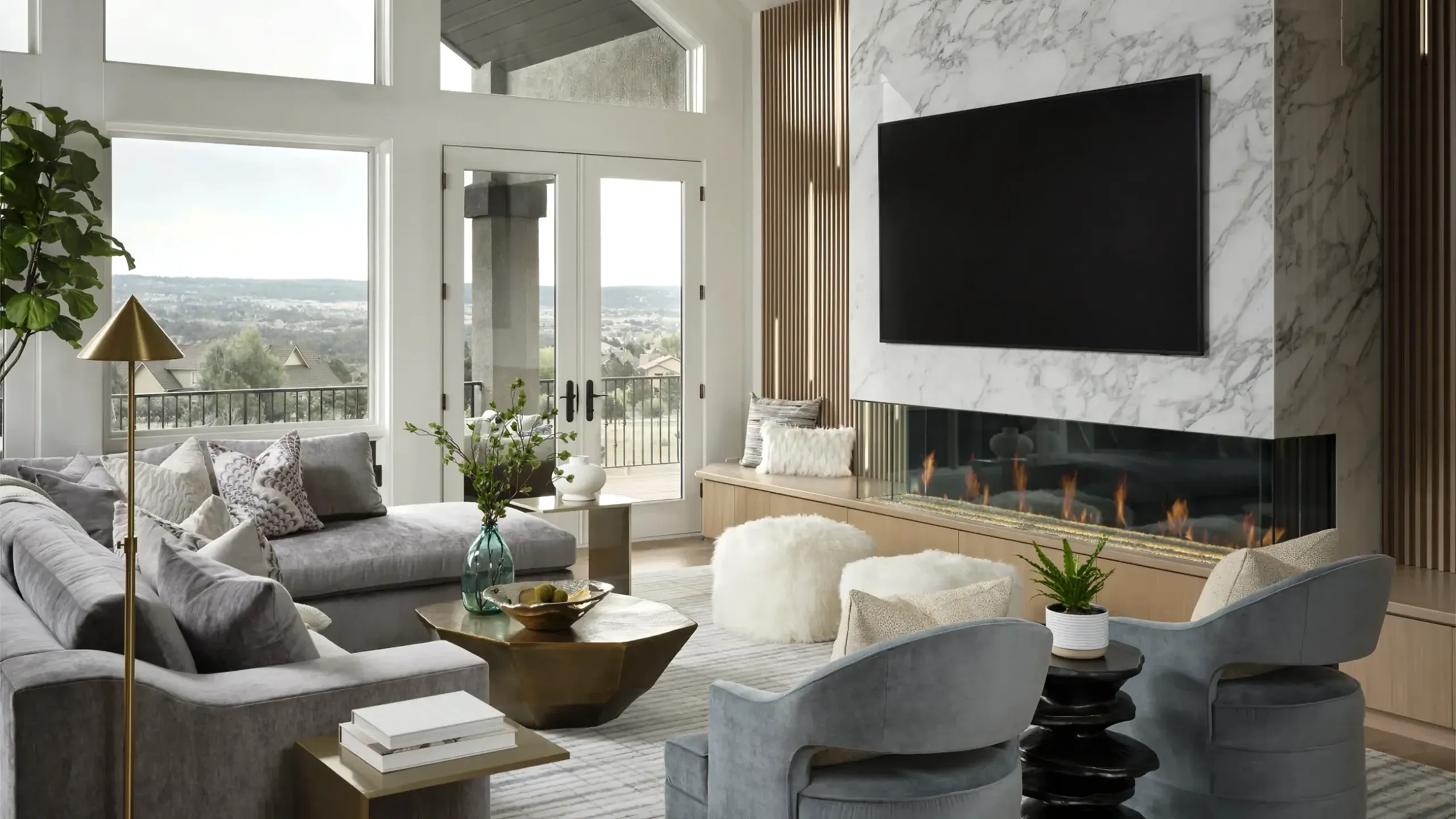 Modern living room with gray sectional sofa, two blue armchairs, marble fireplace, wall-mounted TV, large windows, and gold geometric coffee table.