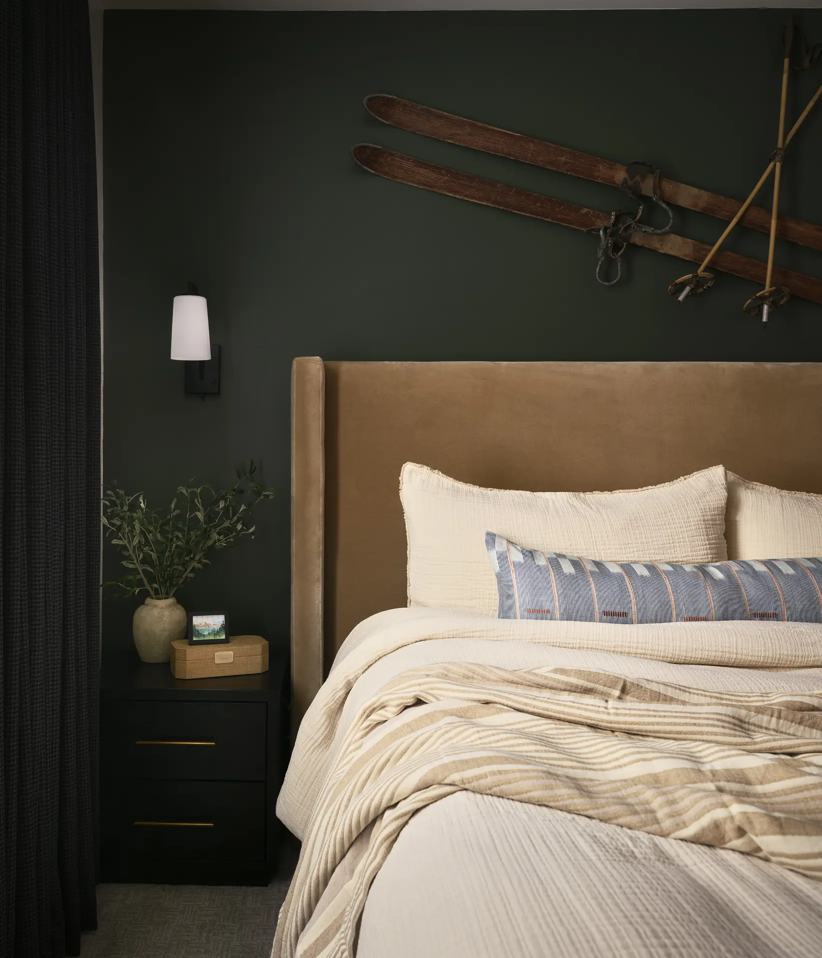 A ski themed bedroom with a dark green accent wall and natural linen bedding
