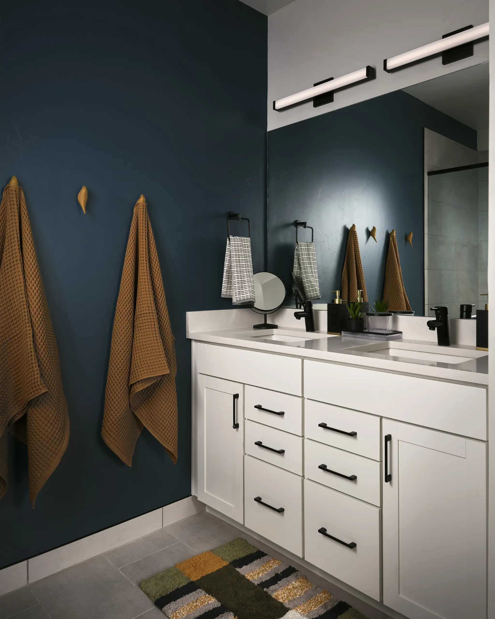 A newly redesigned bathroom with a blue accent wall and white cabinets by Julie Kay Design Studio