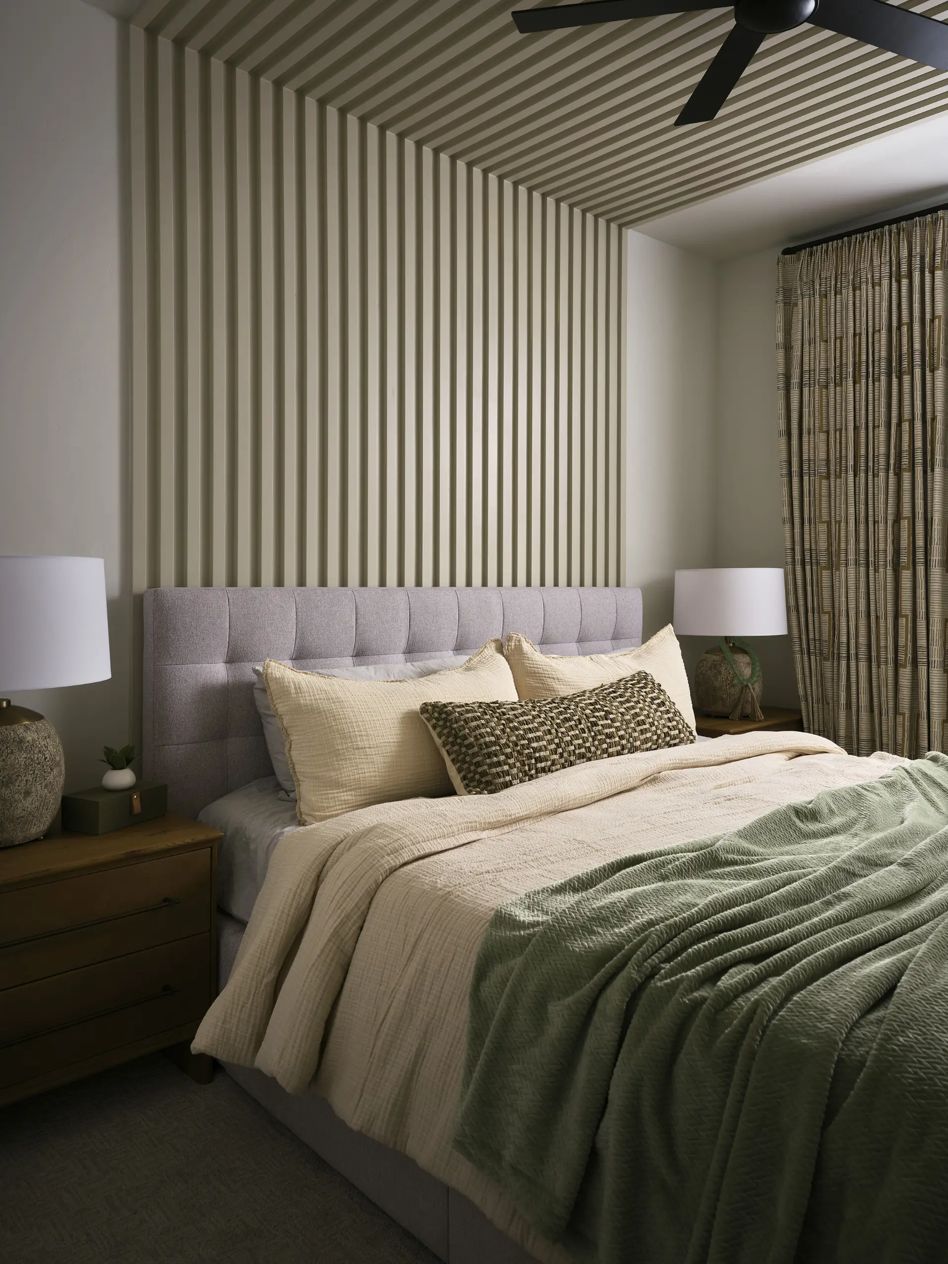 A modern bedroom with a fluted accent wall behind the bed that has sage green bedding