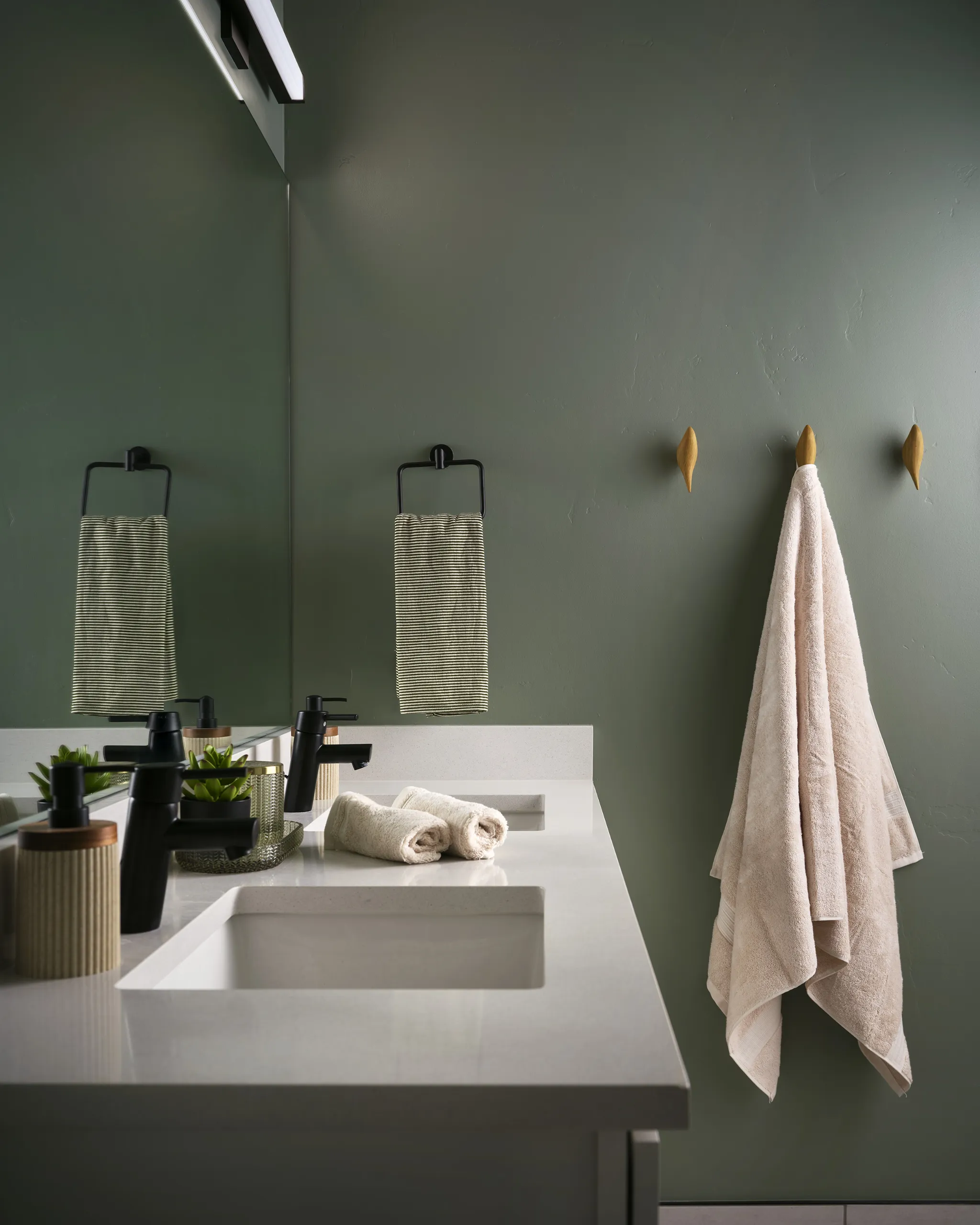 A newly redesigned bathroom with a green accent wall and white cabinets by Julie Kay Design Studio