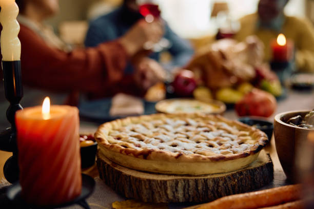 Thanksgiving pie on dining table with family in the background. Close up of traditional pie for Thanksgiving with family in the background. Festive table close-up showing various Thanksgiving desserts, stock pictures, royalty-free photos & images