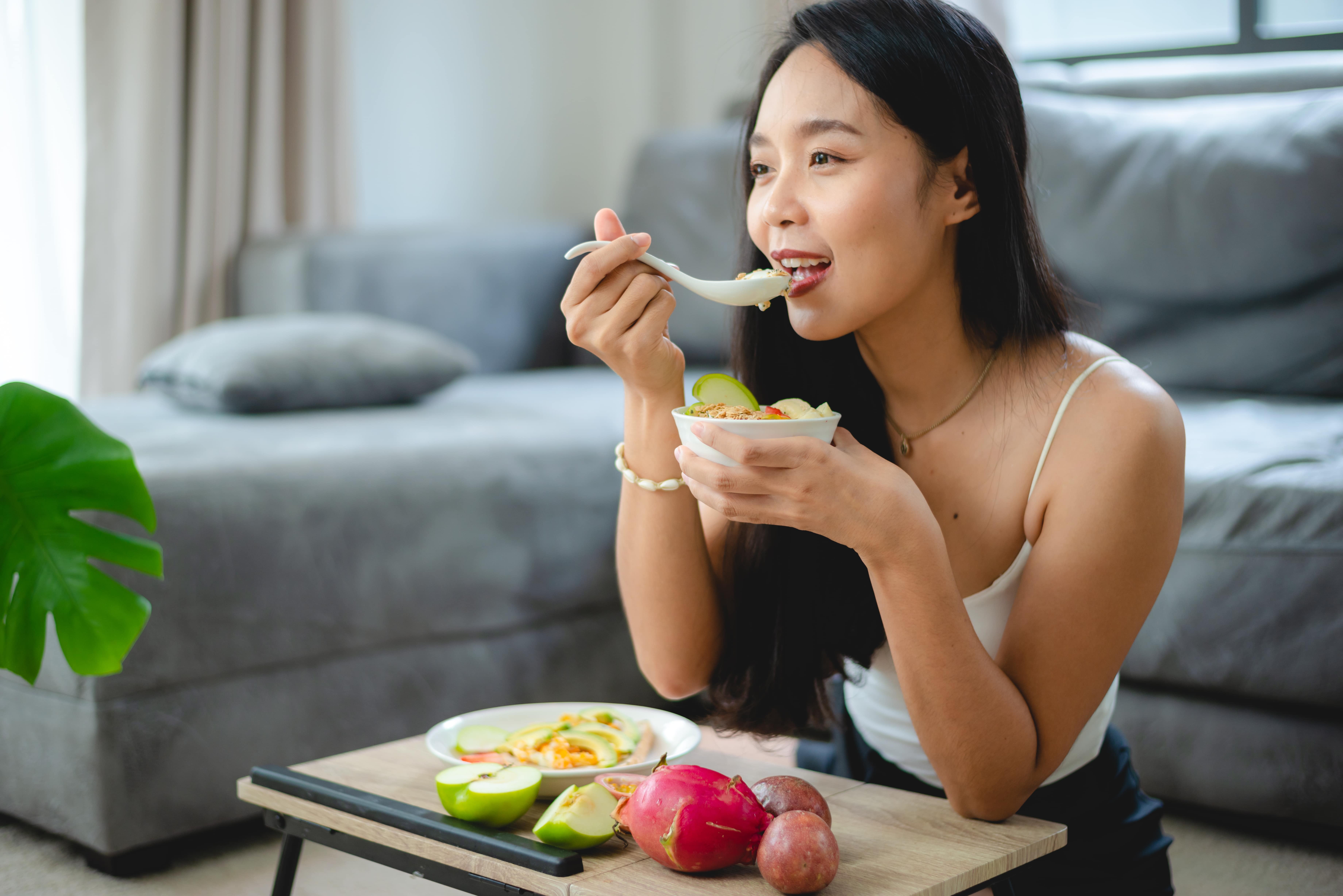 Woman eating a salad at a table with fresh vegetables