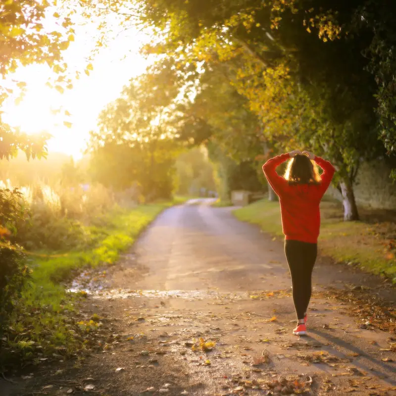 Frau geht bei Sonnenaufgang einen Weg entlang: Symbol für Heilung, Selbstfürsorge und ganzheitliche Gesundheit durch funktionelle Medizin in Berlin.
