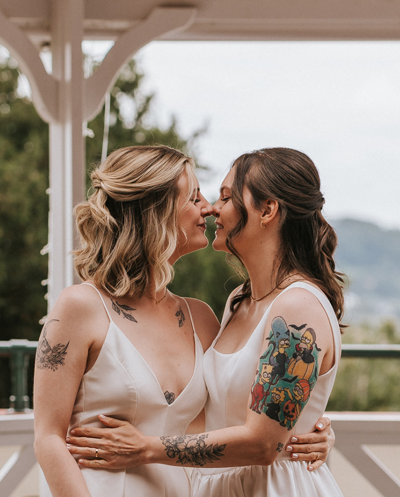 Brides Abi and Jodie sharing a joyful embrace and kiss during their wedding ceremony, captured by celebrant Kate Rostance in an intimate and inclusive celebration.