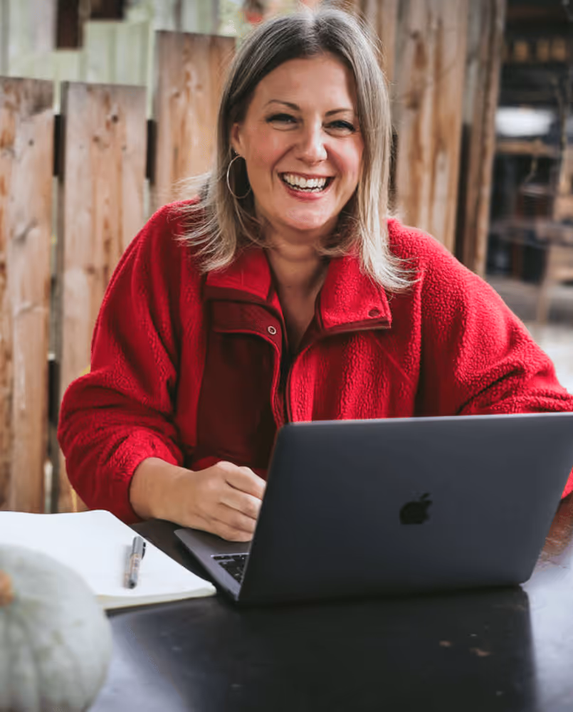 Kate Rostance, wedding celebrant, smiling at her laptop — waiting for you to get in touch.