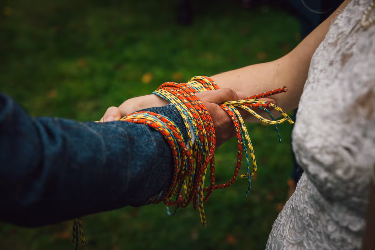 Close-up of a handfasting ceremony where two people’s hands are bound together with colourful climbing ropes, symbolising unity and commitment. The vibrant cords and natural outdoor setting reflect a personal, non-traditional wedding ritual celebrating connection and adventure.