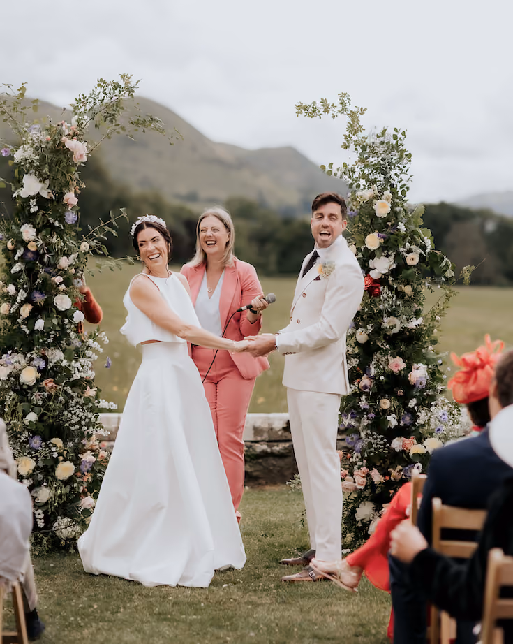 Wedding celebrant Kate Rostance laughing with a couple during their outdoor wedding ceremony at Plas Dinam in Powys, Wales