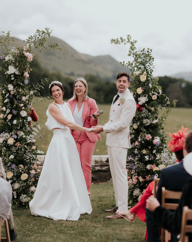 Wedding celebrant Kate Rostance laughing with a couple during their outdoor wedding ceremony at Plas Dinam in Powys, Wales