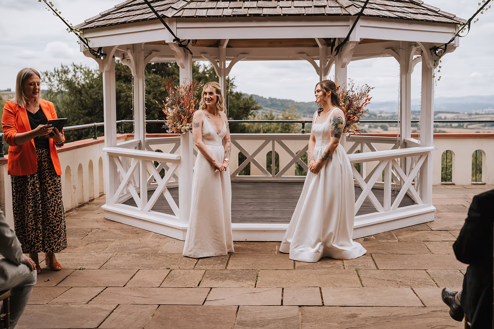 Wedding celebrant Kate Rostance leading the outdoor ceremony at Caer Llan, with brides Abi and Jodie standing together by the gazebo decorated with flowers