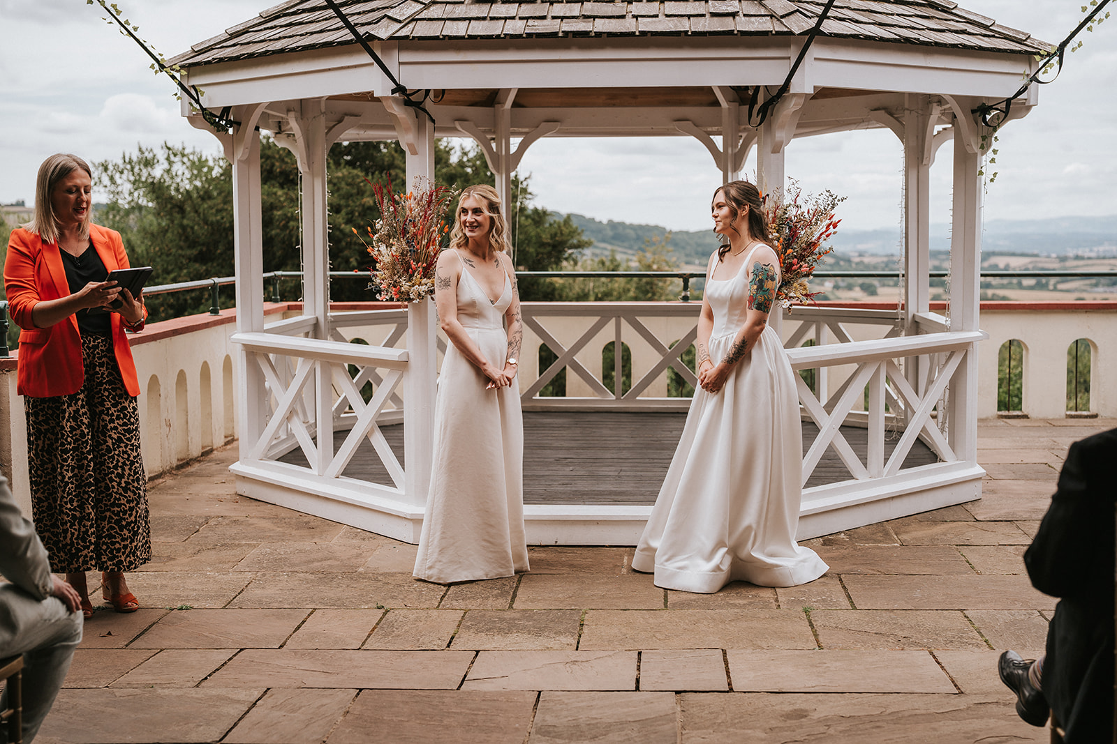 Wedding celebrant Kate Rostance leading the outdoor ceremony at Caer Llan, with brides Abi and Jodie standing together by the gazebo decorated with flowers