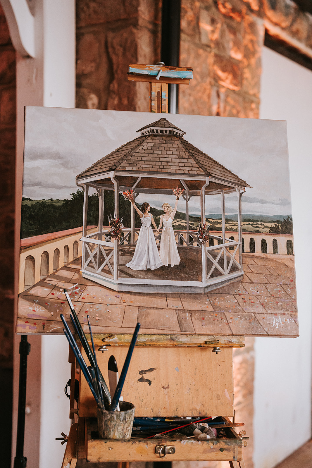 Live wedding painting at Caer Llan showing brides Abi and Jodie celebrating in the gazebo, created by an artist during their ceremony.