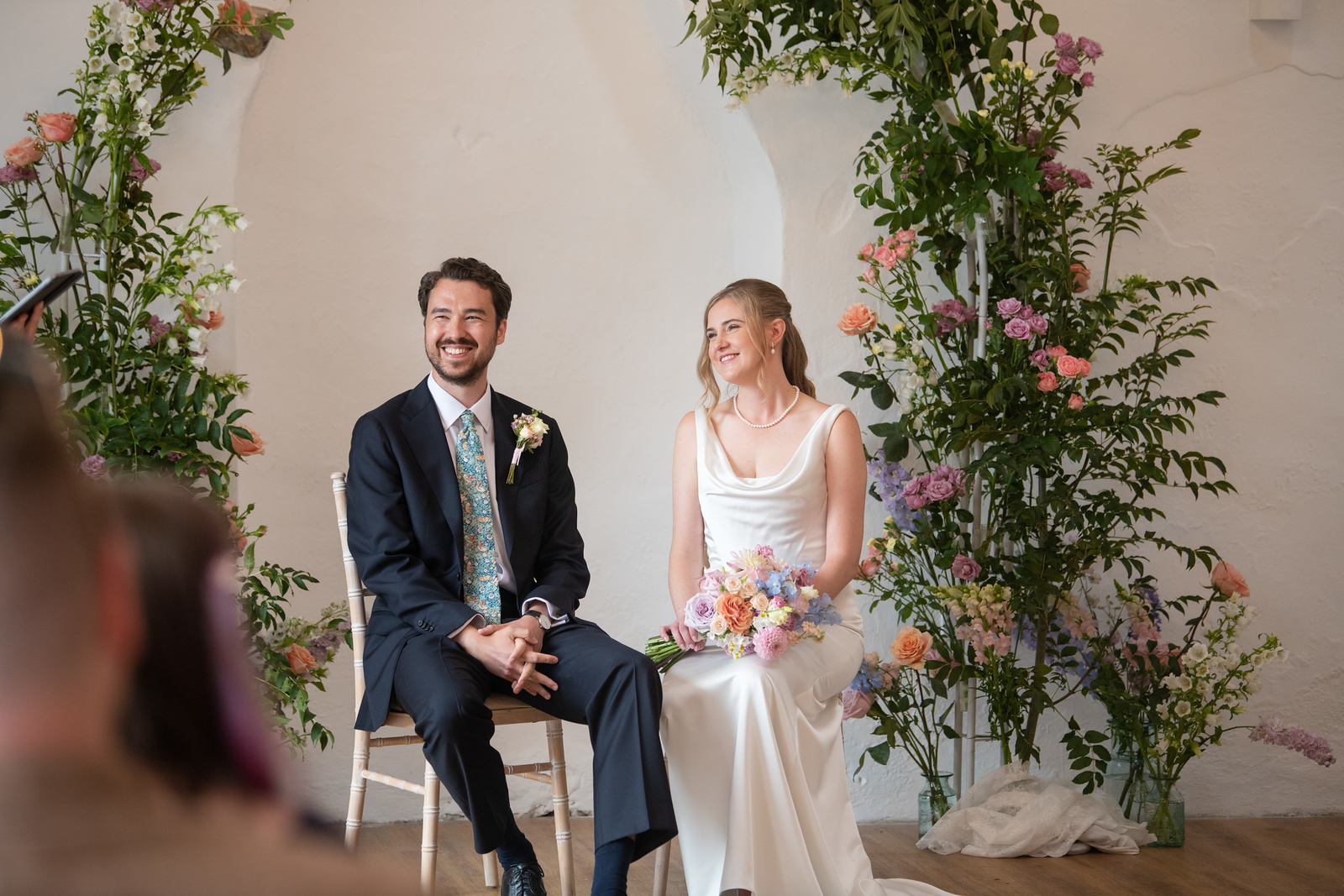 Bride Emily and groom David smiling during their wedding ceremony at Talhenbont Hall in the Llyn Peninsula, with celebrant Kate Rostance leading a joyful and relaxed moment.