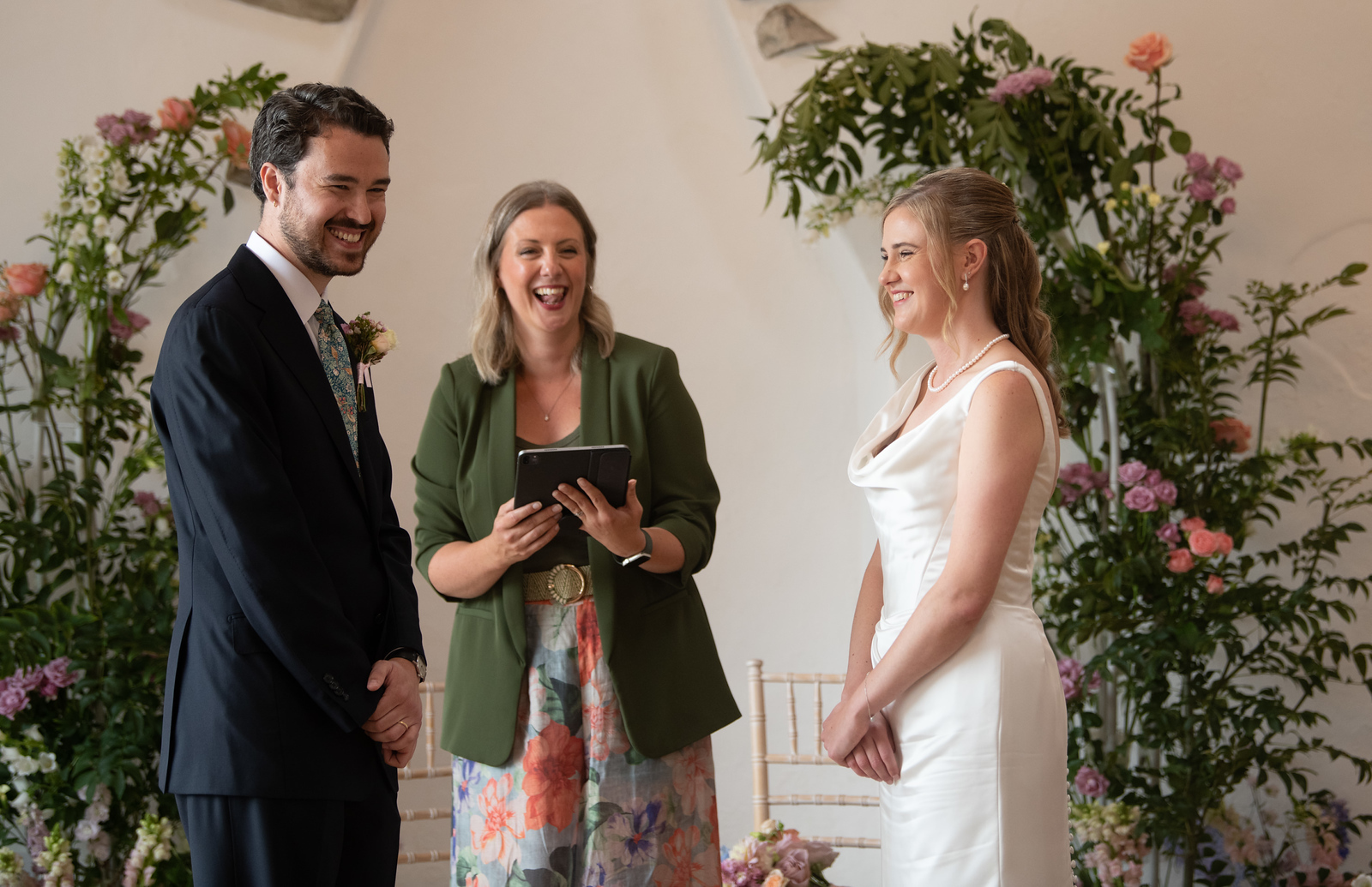 Bride and groom Emily and David share laughter with celebrant Kate Rostance during their personal wedding ceremony at Talhenbont Hall, North Wales