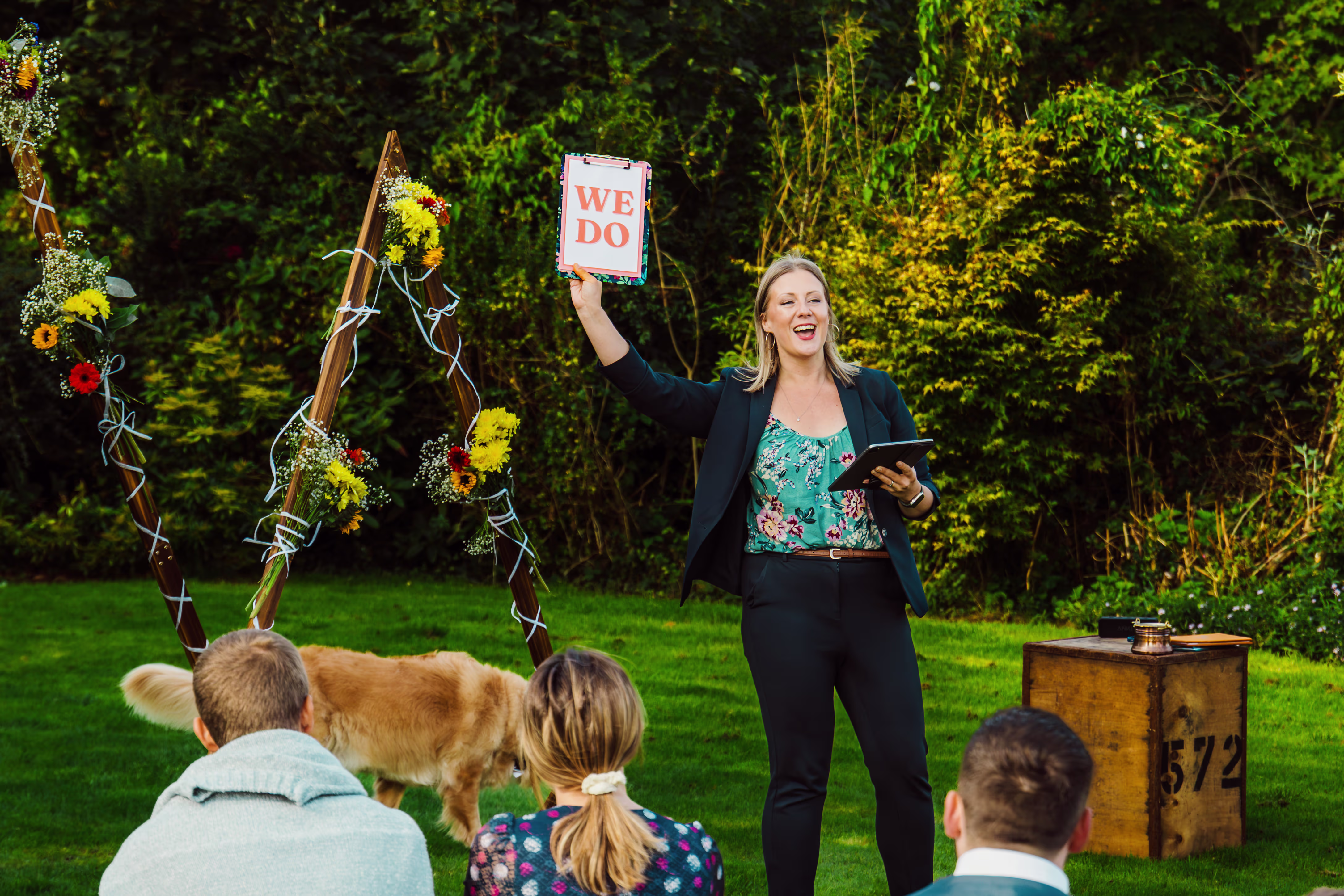 Celebrant Kate Rostance leads Elena and Graham’s Anglesey wedding ceremony with guests and dog on the lawn.