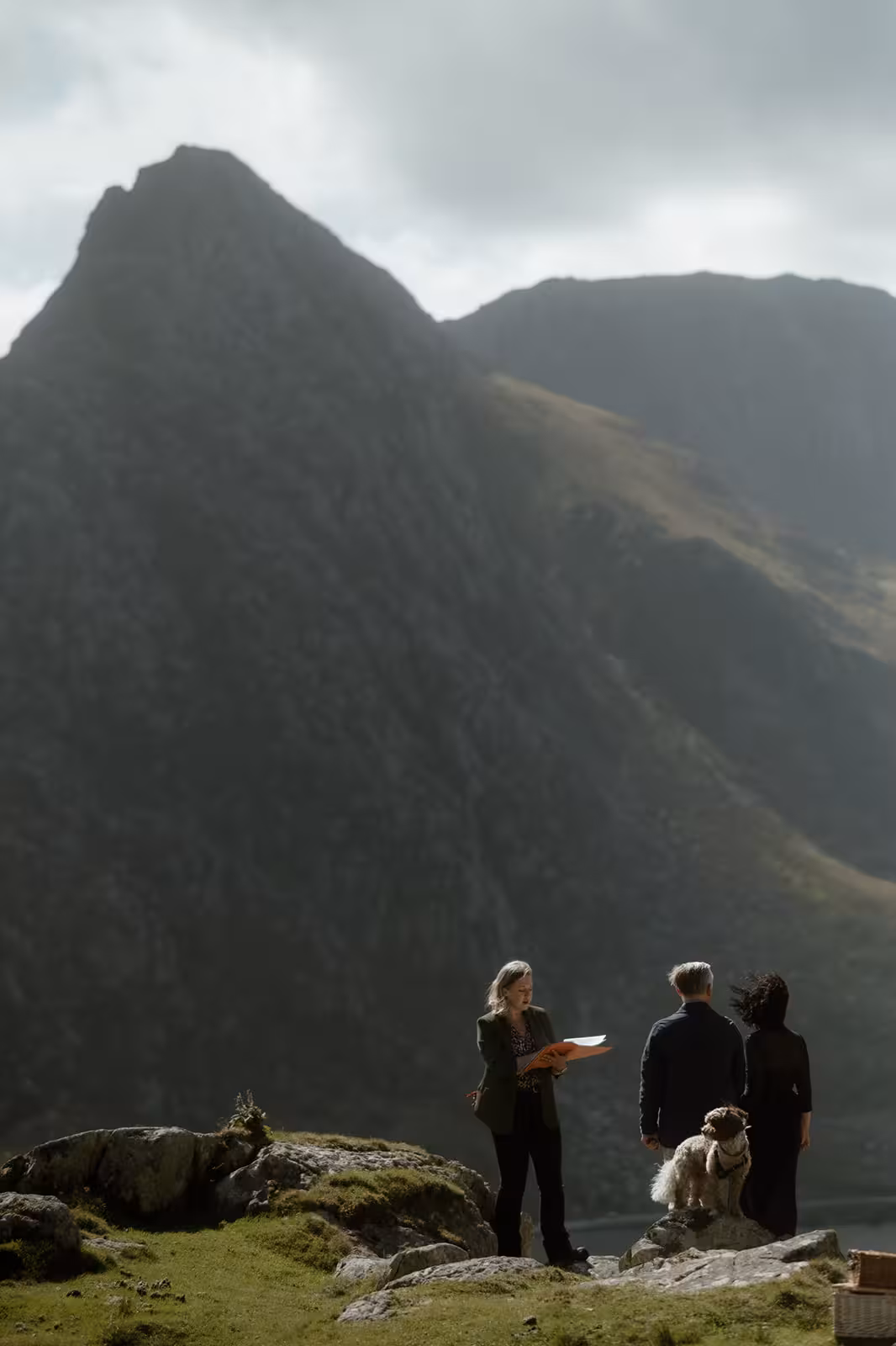 The celebrant leads Gina and Paul’s handfasting ceremony on Pen y Ole Wen, with their dog Coco nearby and the dramatic mountain peaks of Eryri in the background.
