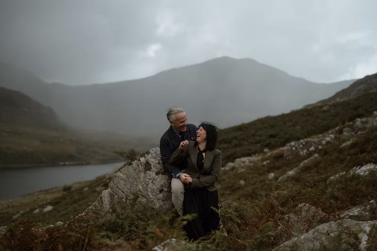 Paul and Gina share a tender, playful moment on the rocks overlooking Llyn Ogwen in Eryri, with mist rolling through the mountains after their ceremony.