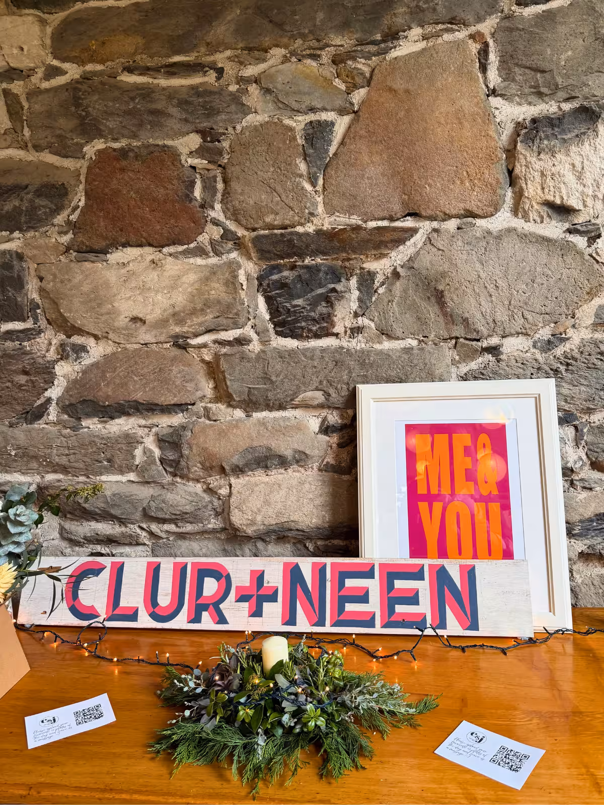 Rustic wedding ceremony setup at Llyn Gwynant Barns with wooden ladder, greenery, flowers and painted signs reading ‘C&J’ and ‘us’ for Clair and Janine’s celebration