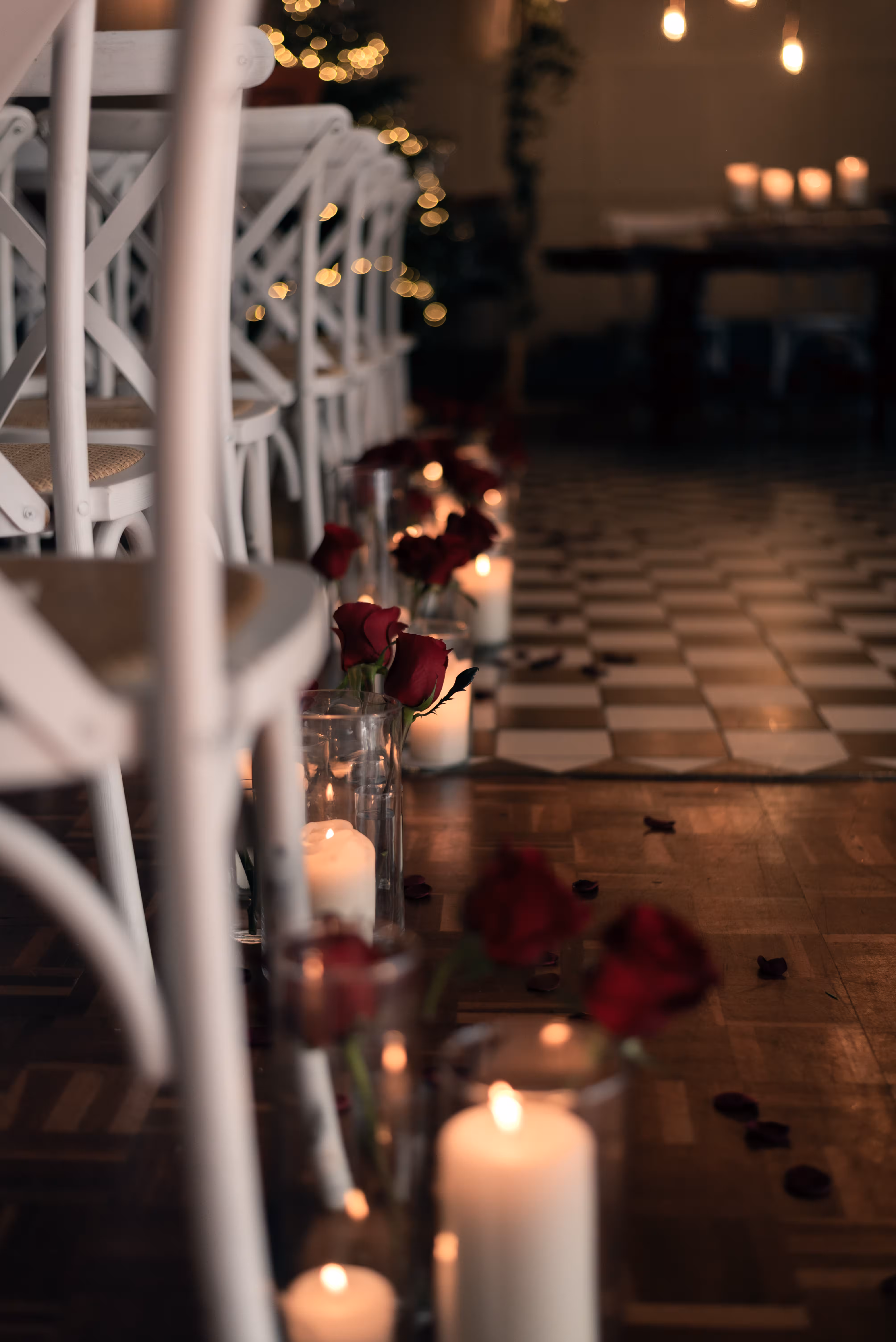 Candlelit ceremony aisle decorated with red roses, glass candles and checkerboard flooring for a winter Humanist wedding at Larkspur Lodge.