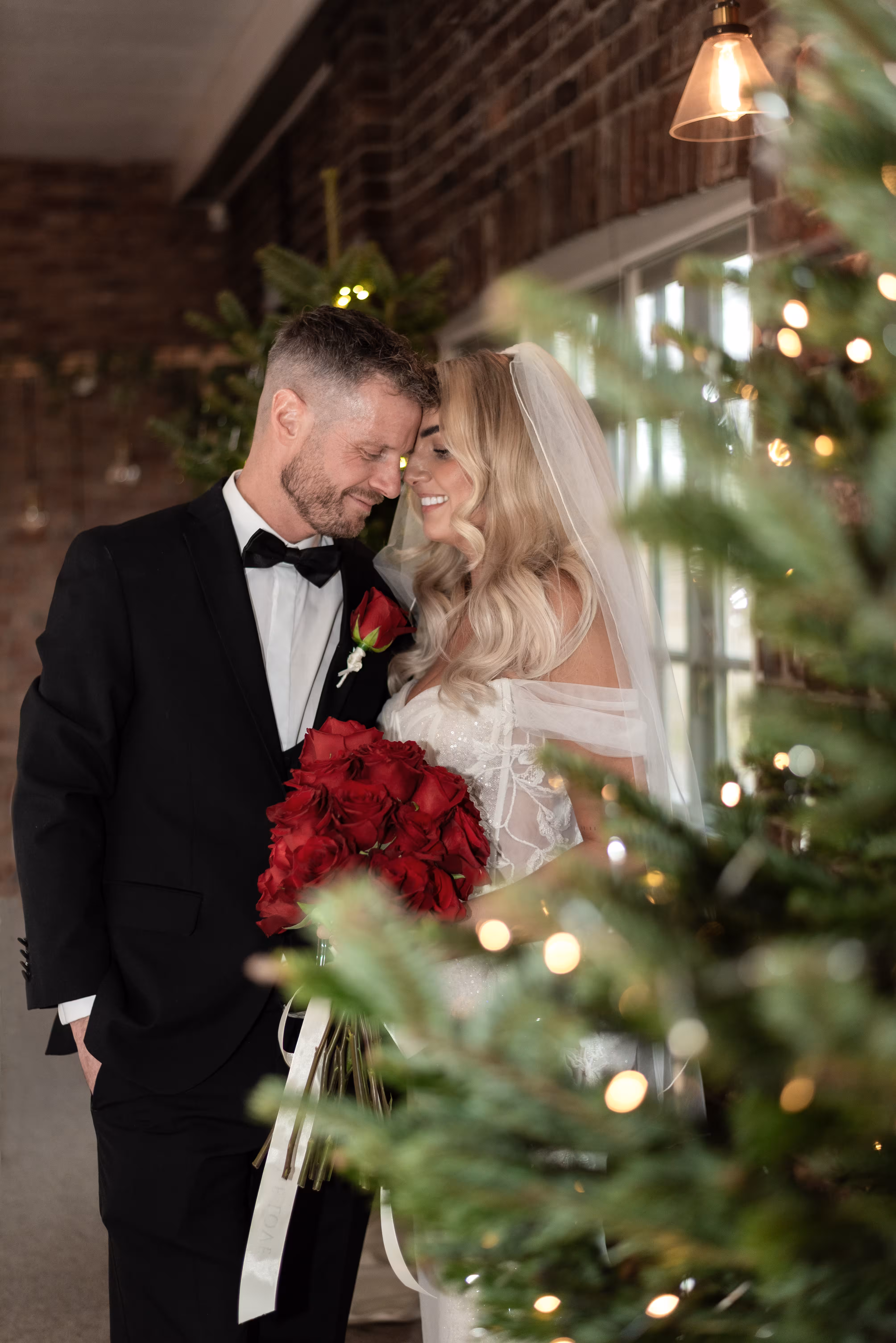 Couple share a tender moment at their Larkspur Lodge wedding with Christmas trees and fairy lights