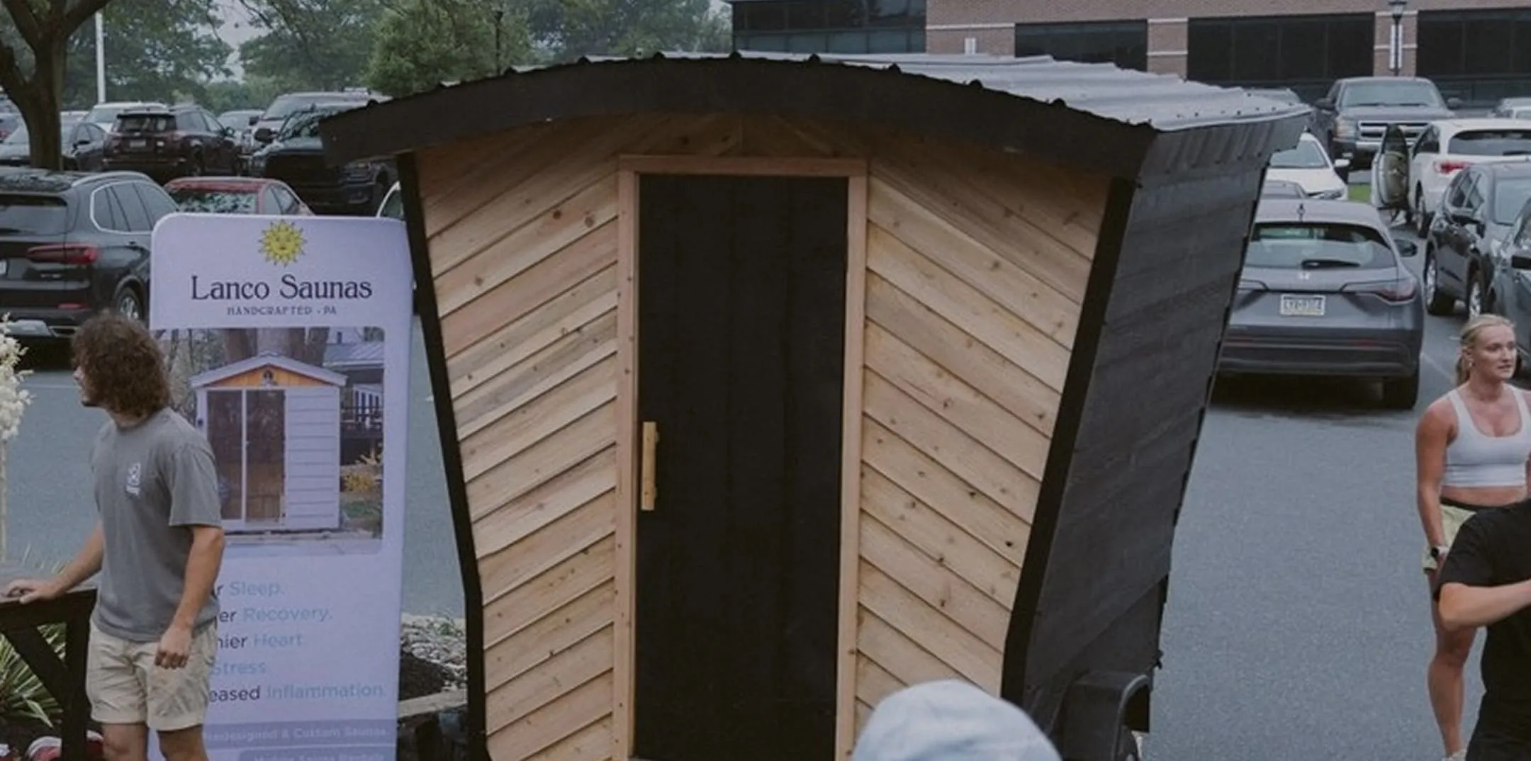 A group of people standing around a wooden sauna.