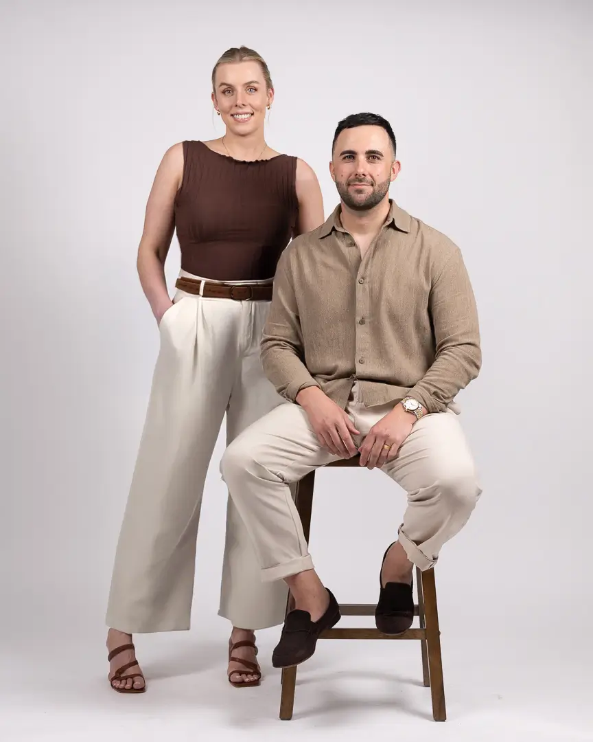 Kate Smith and Cameron Gerardis, co-founders of LikeSilk Building, standing together in stylish casual attire, exuding confidence and approachability against a plain background.