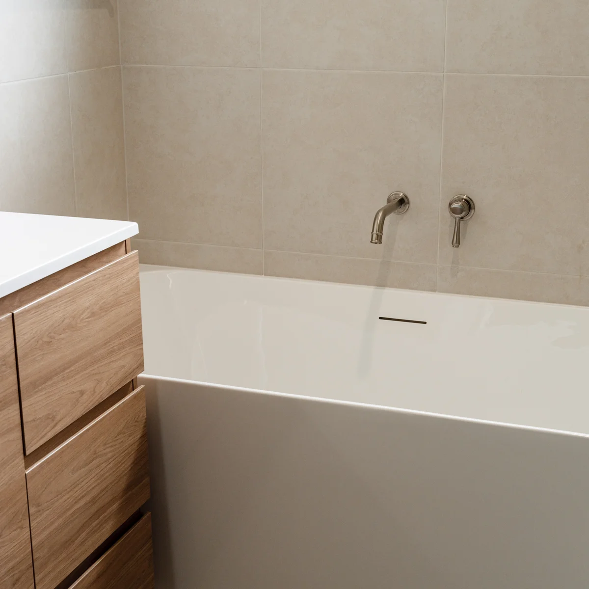 Freestanding white bathtub with wall-mounted spout beside timber vanity in renovated bathroom