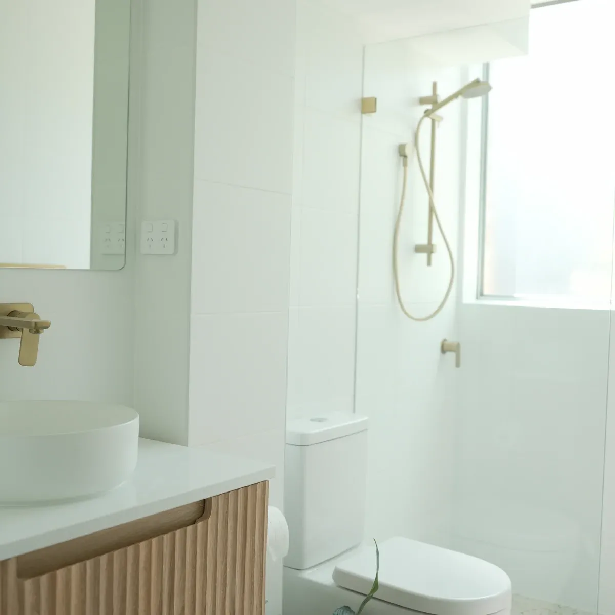 Modern white bathroom renovation featuring timber vanity with brass tapware, freestanding bathtub and indoor plant - North Shore Sydney