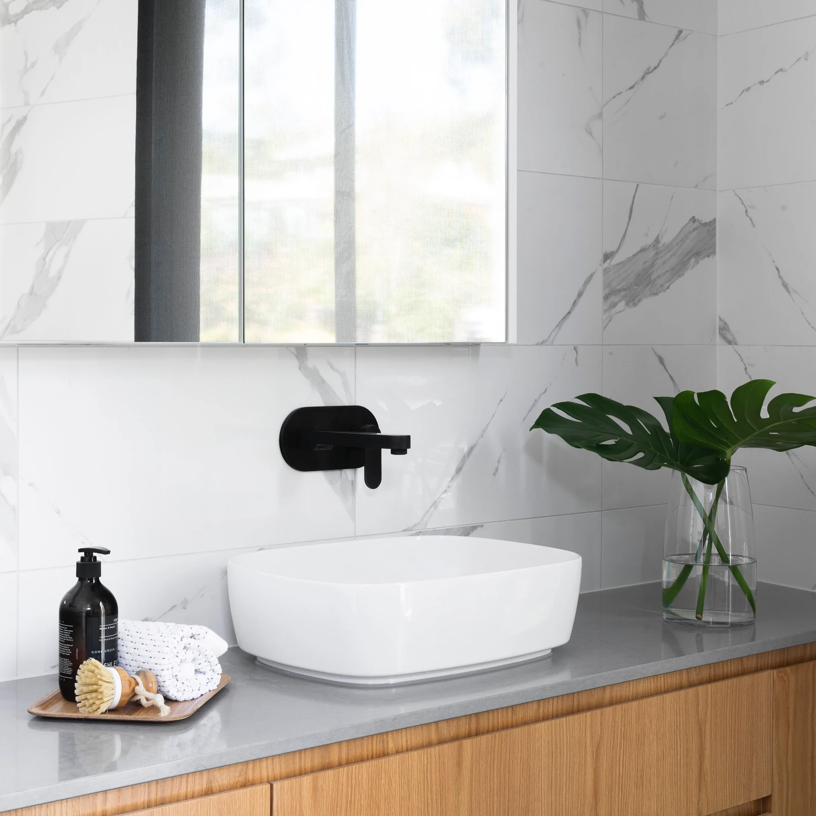 Modern bathroom with marble-look tiles, timber vanity, black tapware and above-counter basin