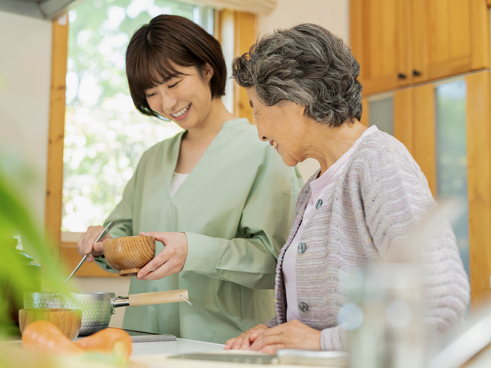帰省した娘が台所で高齢の母と会話しながら料理をする様子