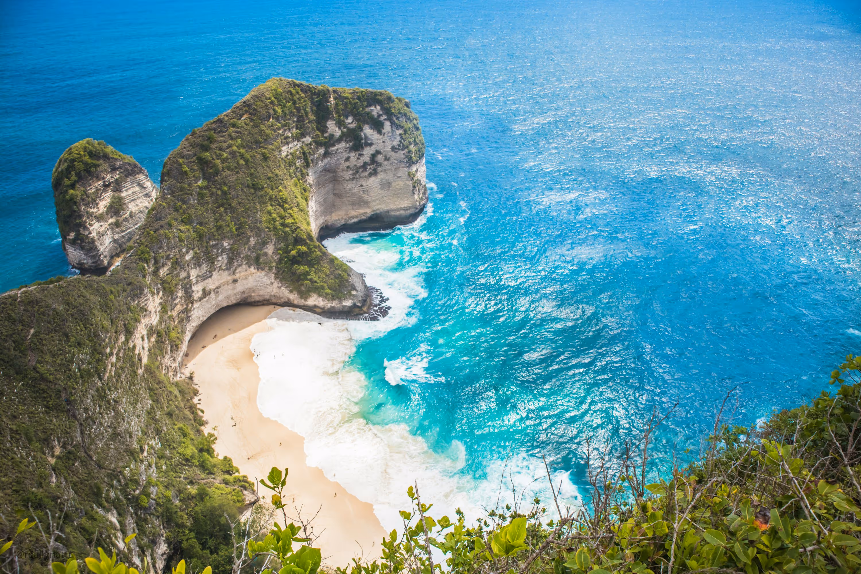 an aerial view of a sandy beach with two large rocks sticking out of the water